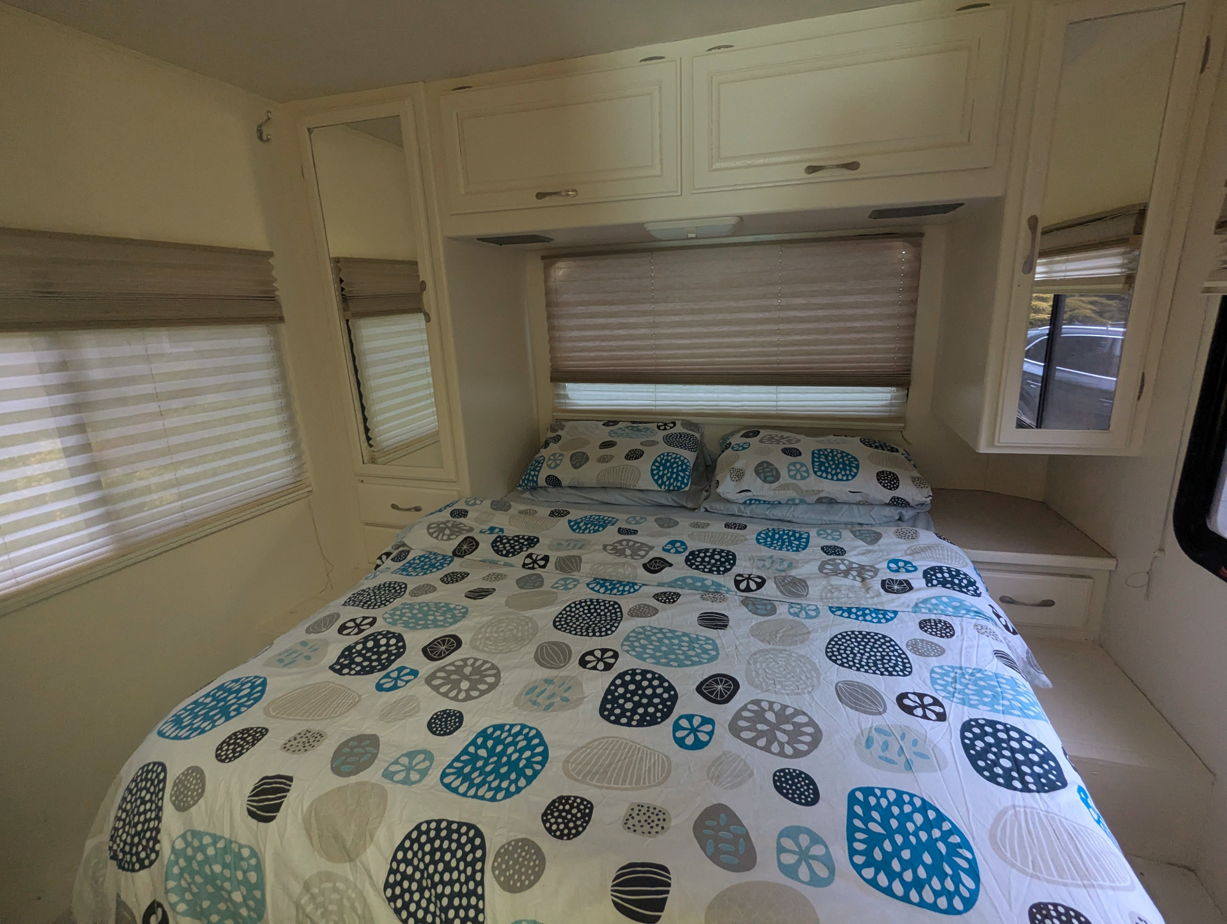 Cozy RV rental bedroom featuring patterned bedding, overhead cabinets, and blinds, perfect for a comfortable stay.. Four Winds Chateau Sport 2005