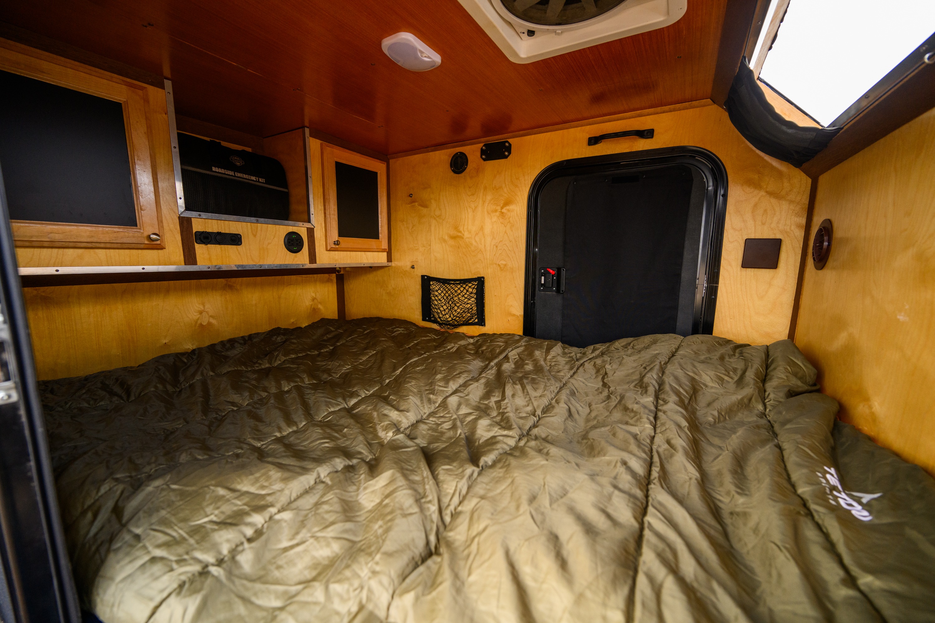 Inside a compact RV rental's cozy sleeping area, featuring a large olive green bed, wood interior, and functional built-ins.. Venture XTR 2022