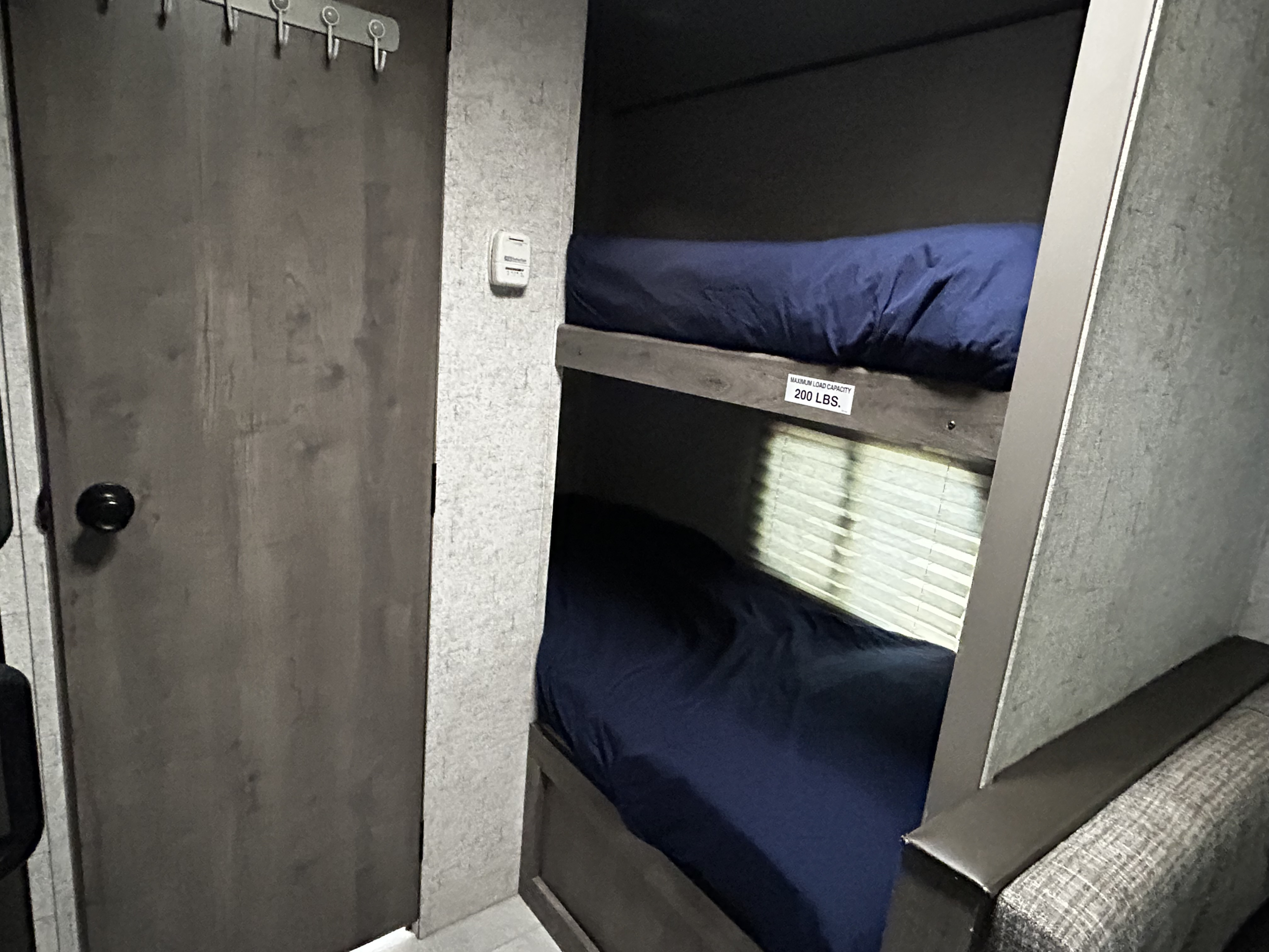 This RV rental interior features compact bunk beds with blue sheets, a door with hooks, and a 200 lb. weight limit on the top bunk.. Coachmen Apex Nano 2020