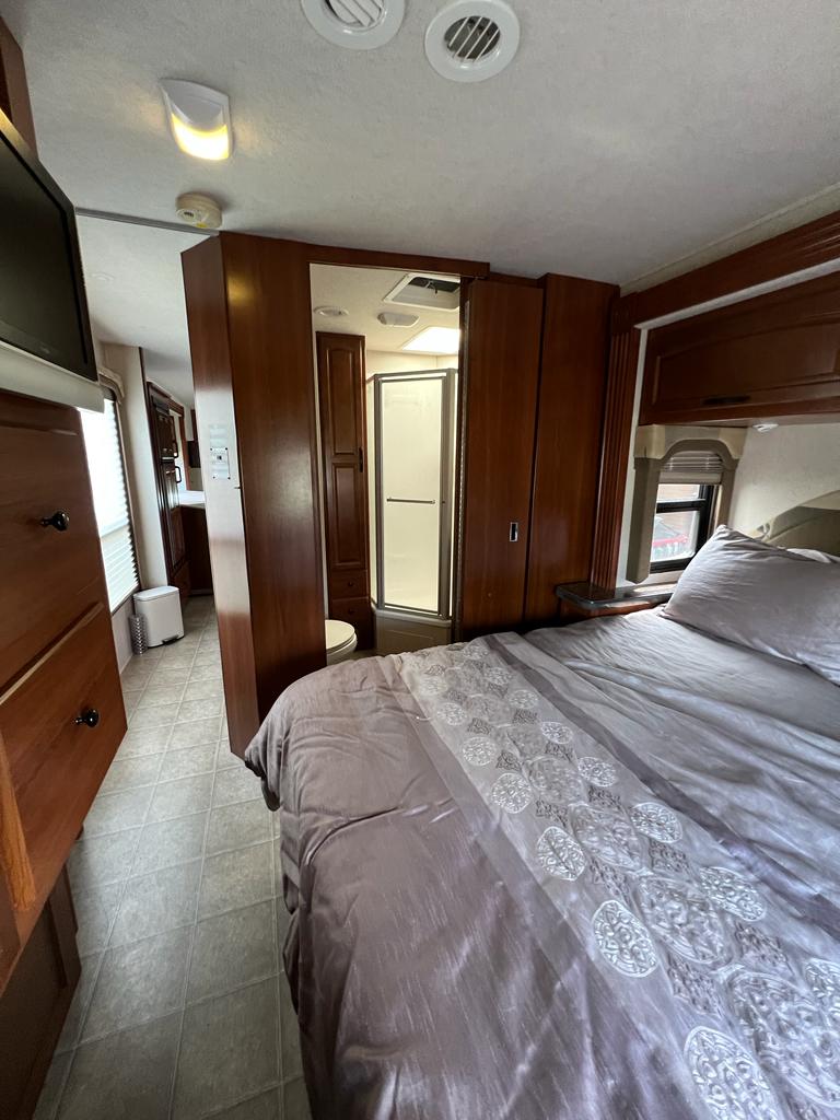 An RV rental interior view: a bedroom with a bed and dresser, leading to a bathroom complete with a shower and toilet.. Tioga Tioga Motorhome 2009
