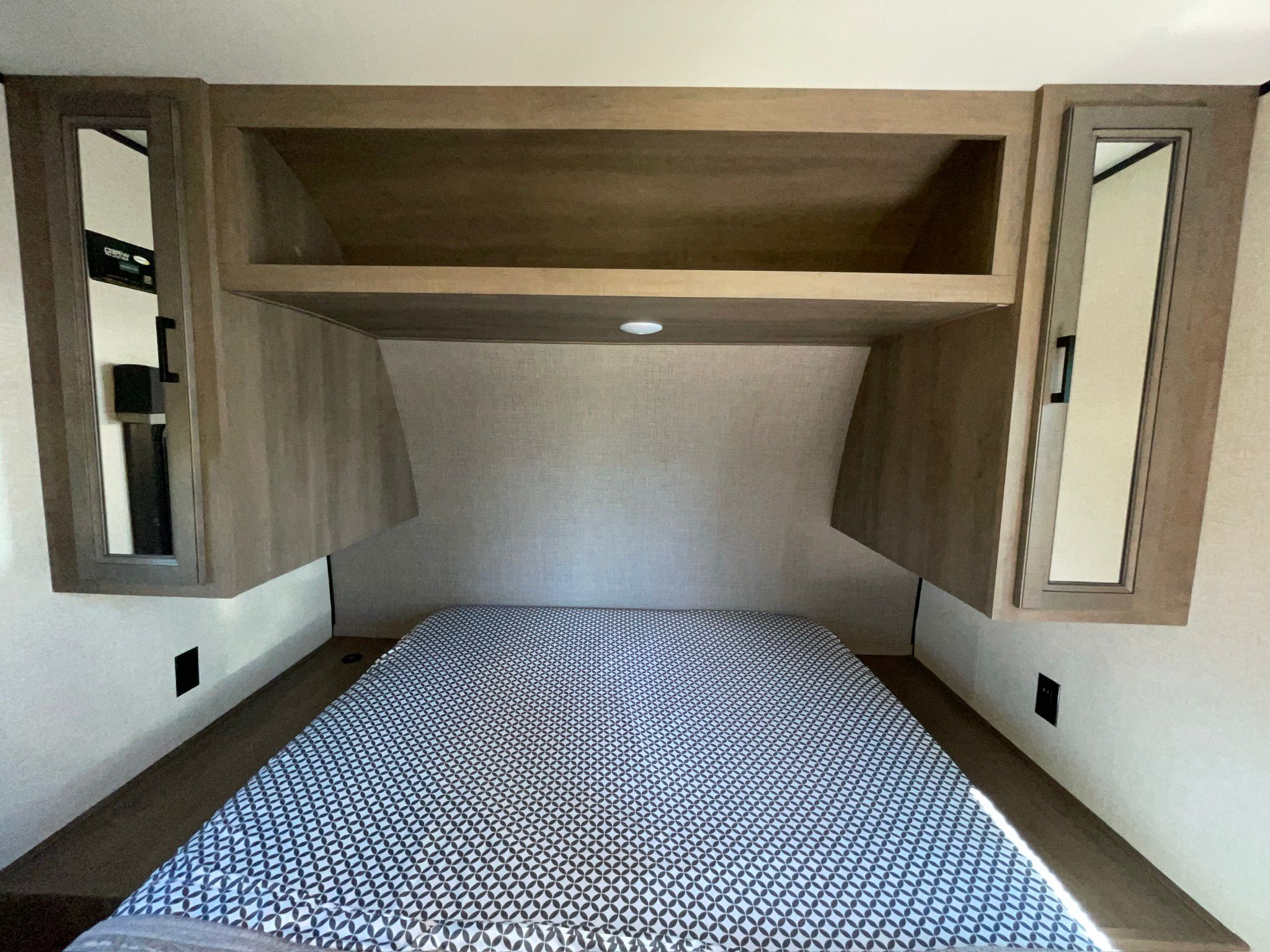 An RV rental's cozy bedroom features a bed with patterned cover, overhead storage, mirrored cabinets, and charging ports.. Starcraft Autumn Ridge 2023