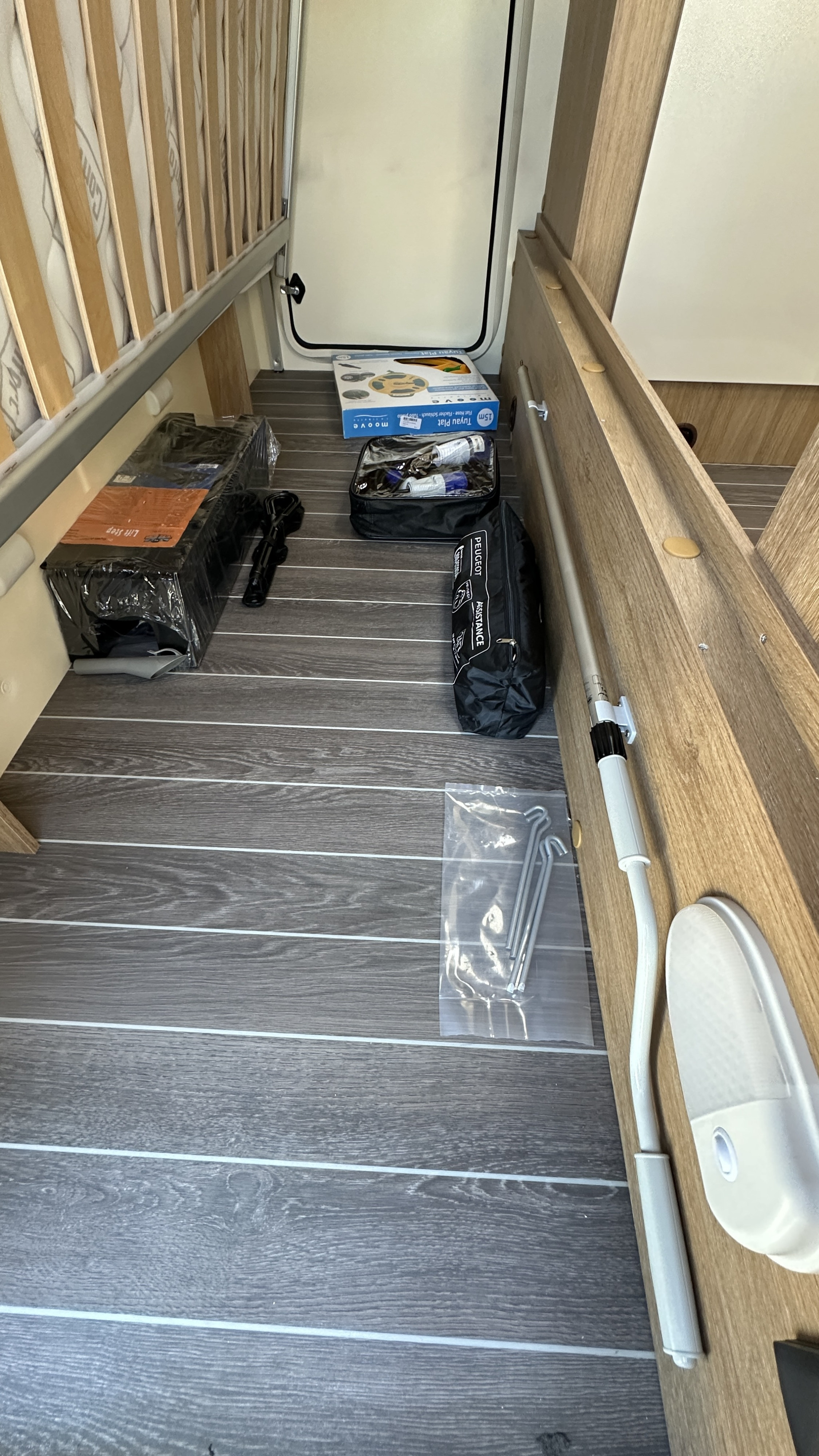RV rental under-bed storage filled with camping essentials: a step, flat hose, assistance kit, and metal stakes on wood flooring.. CI HORON 77M 2023