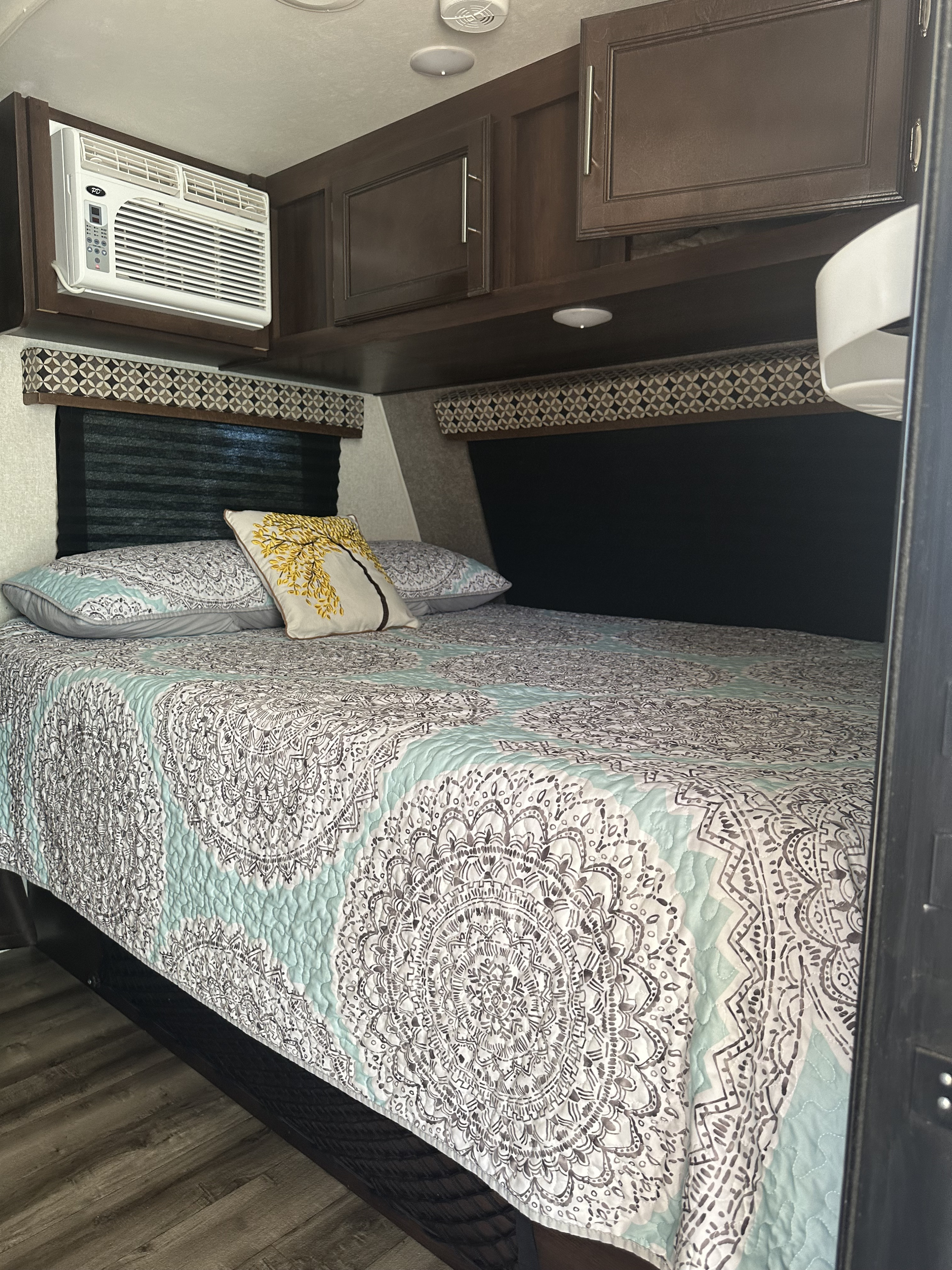 Cozy RV rental bedroom with patterned bedspread, overhead cabinets, and an AC unit for comfort.. Jayco Jay Flight SLX 2019