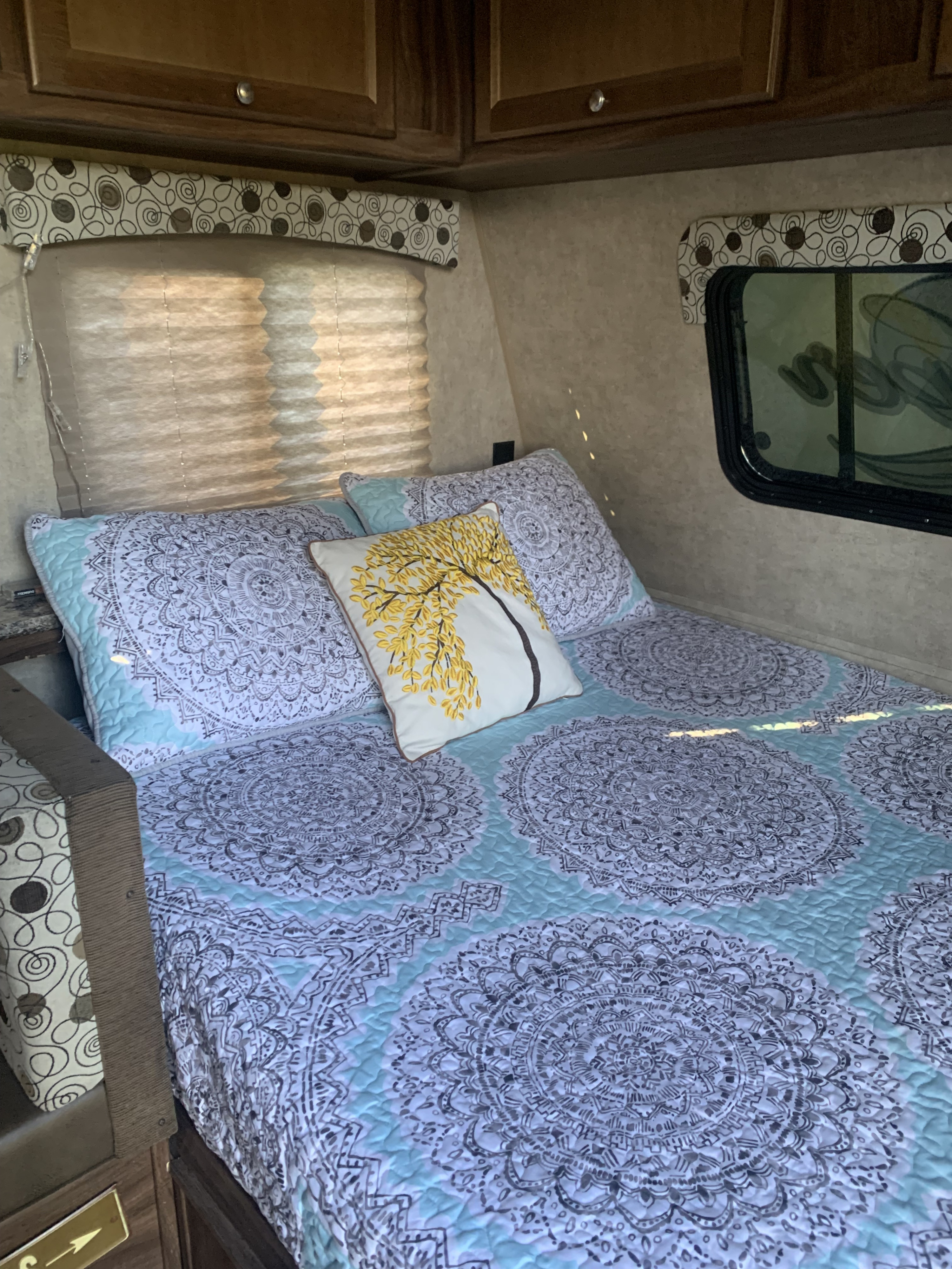 Cozy RV rental bedroom featuring light blue and white mandala bedding, a yellow tree pillow, and window blinds.. Coachmen Clipper ultra lite 2017
