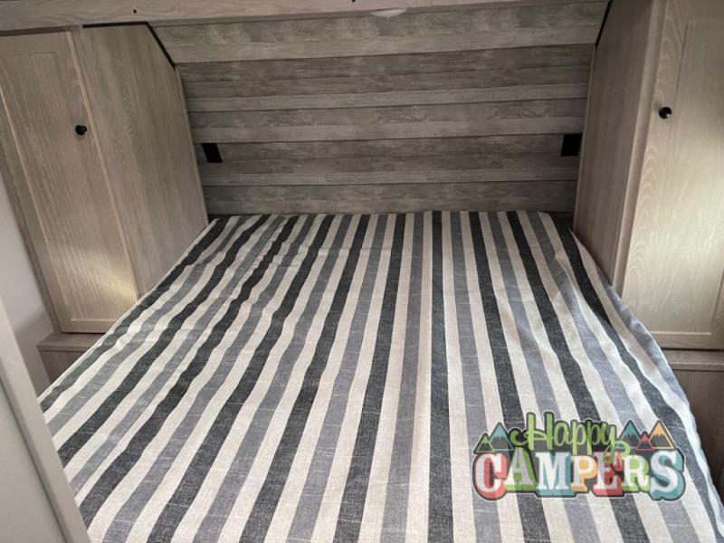 RV rental bedroom: Striped bed between light wood cabinets and a wood-paneled wall. A cozy space for campers.. Riverside RV Intrepid 2023