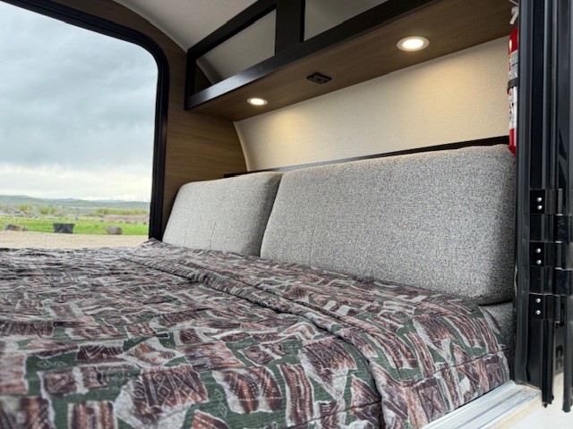 Cozy RV rental interior with a made bed and scenic outdoor views from the window. Perfect for mobile adventures.. Braxton Creek Bushwhacker 10HD Radical 2024