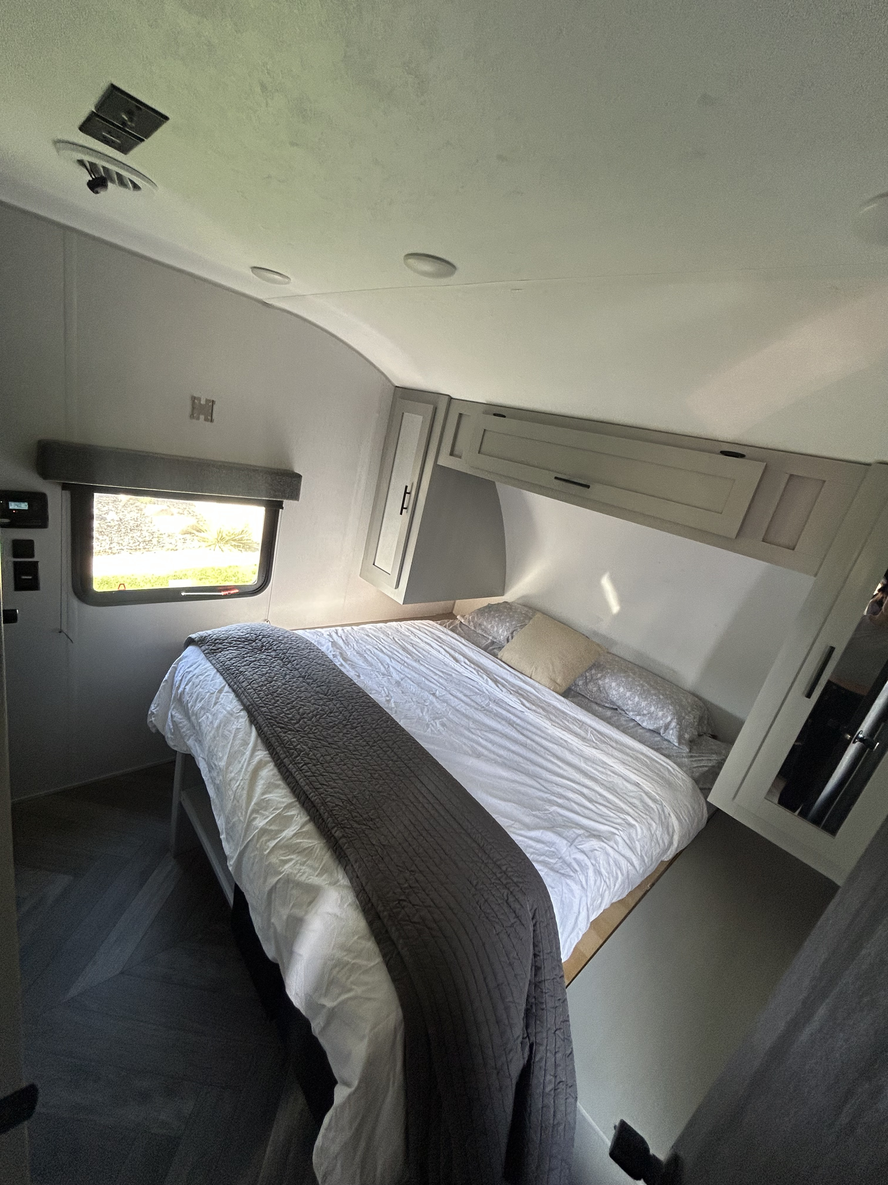 Bright RV rental bedroom featuring a clean bed, overhead cabinets, window, and wall-mounted TV bracket.. Forest River Salem 2021