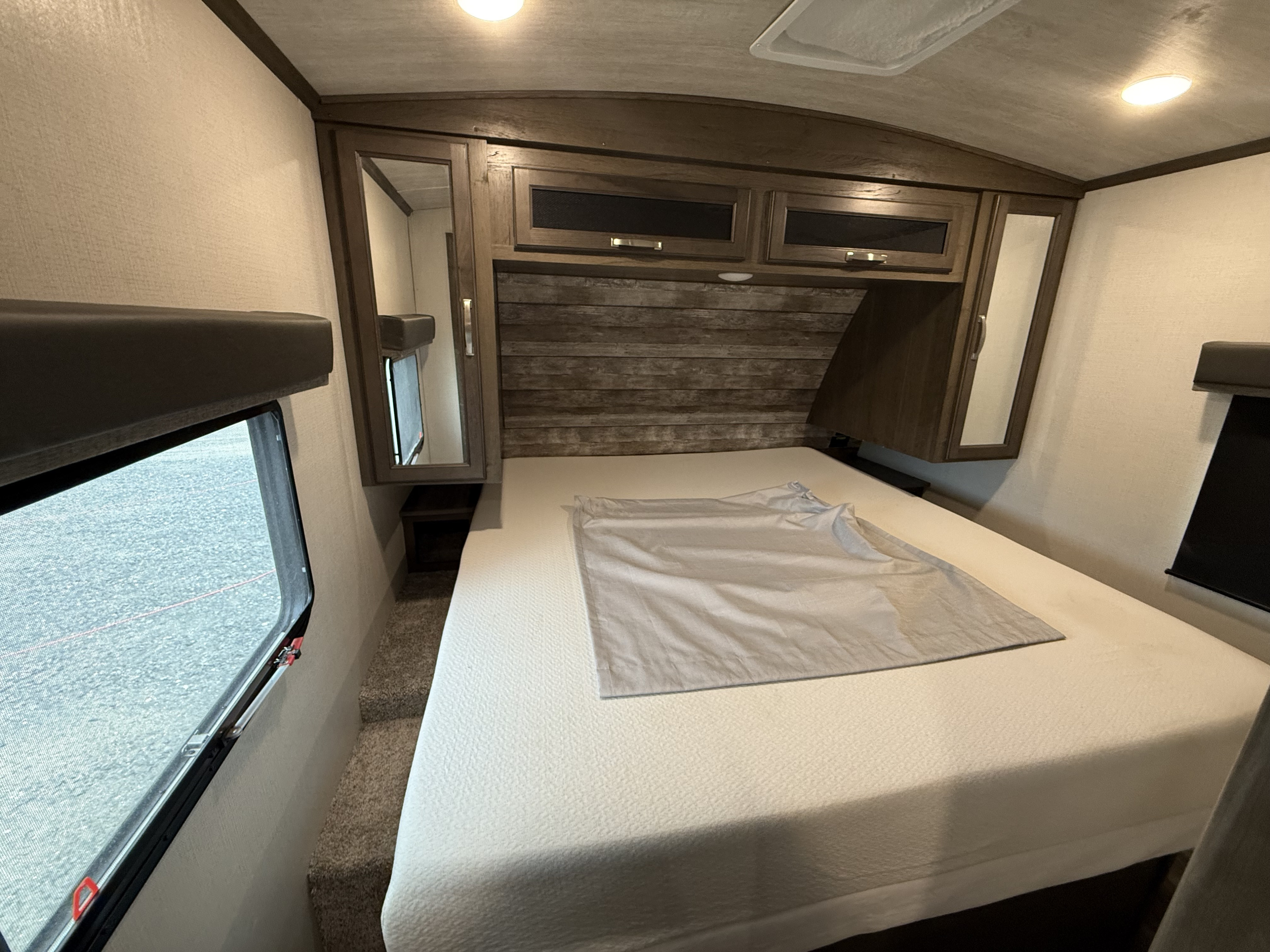 Cozy RV rental bedroom featuring a full bed, built-in cabinets, planked headboard, and side window.. Keystone RV Cougar 2022