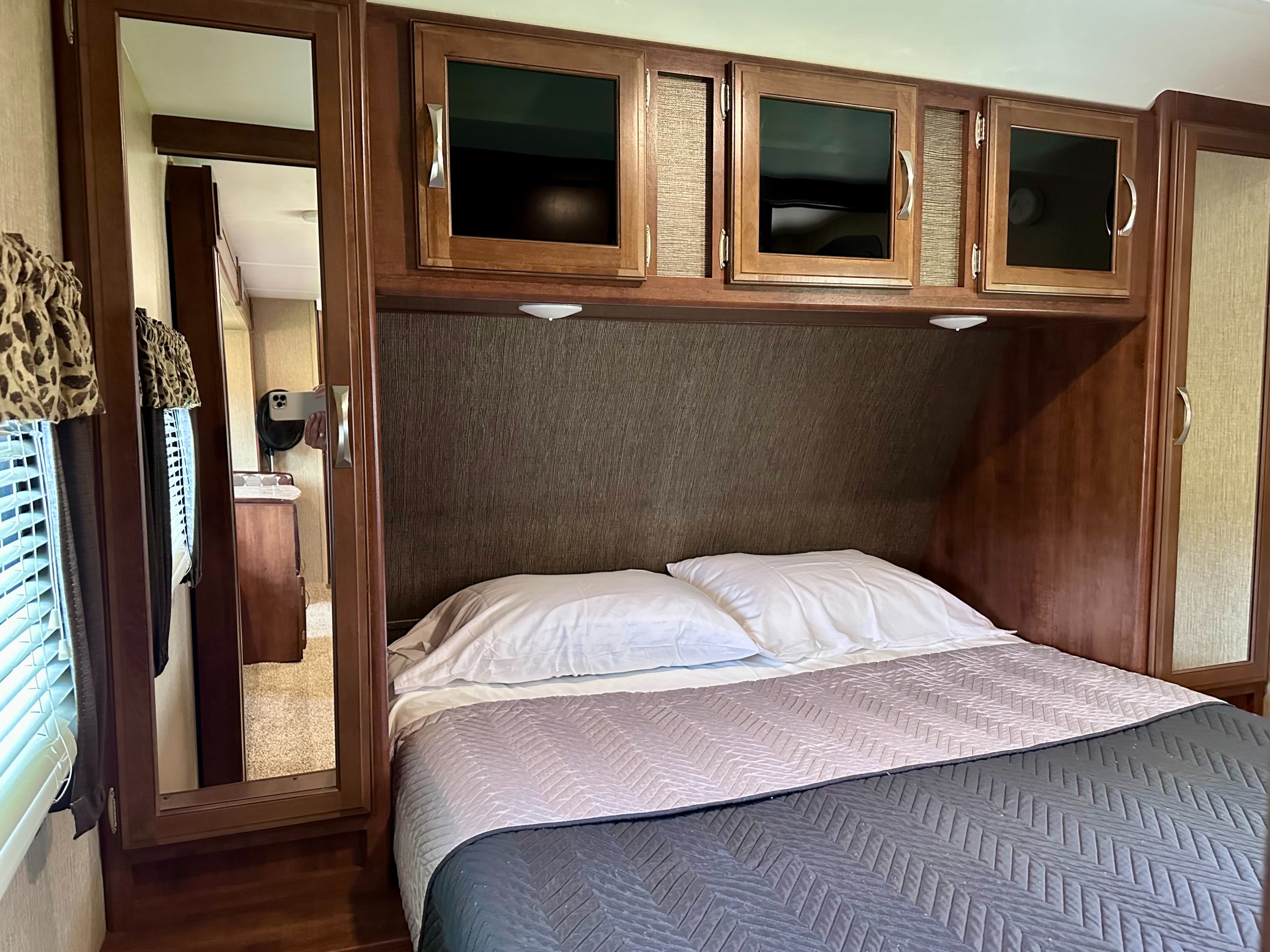 Cozy RV bedroom with a comfortable bed, overhead cabinets, and a full-length mirror, ideal for your rv rental.. Keystone Ultra Lite 2017