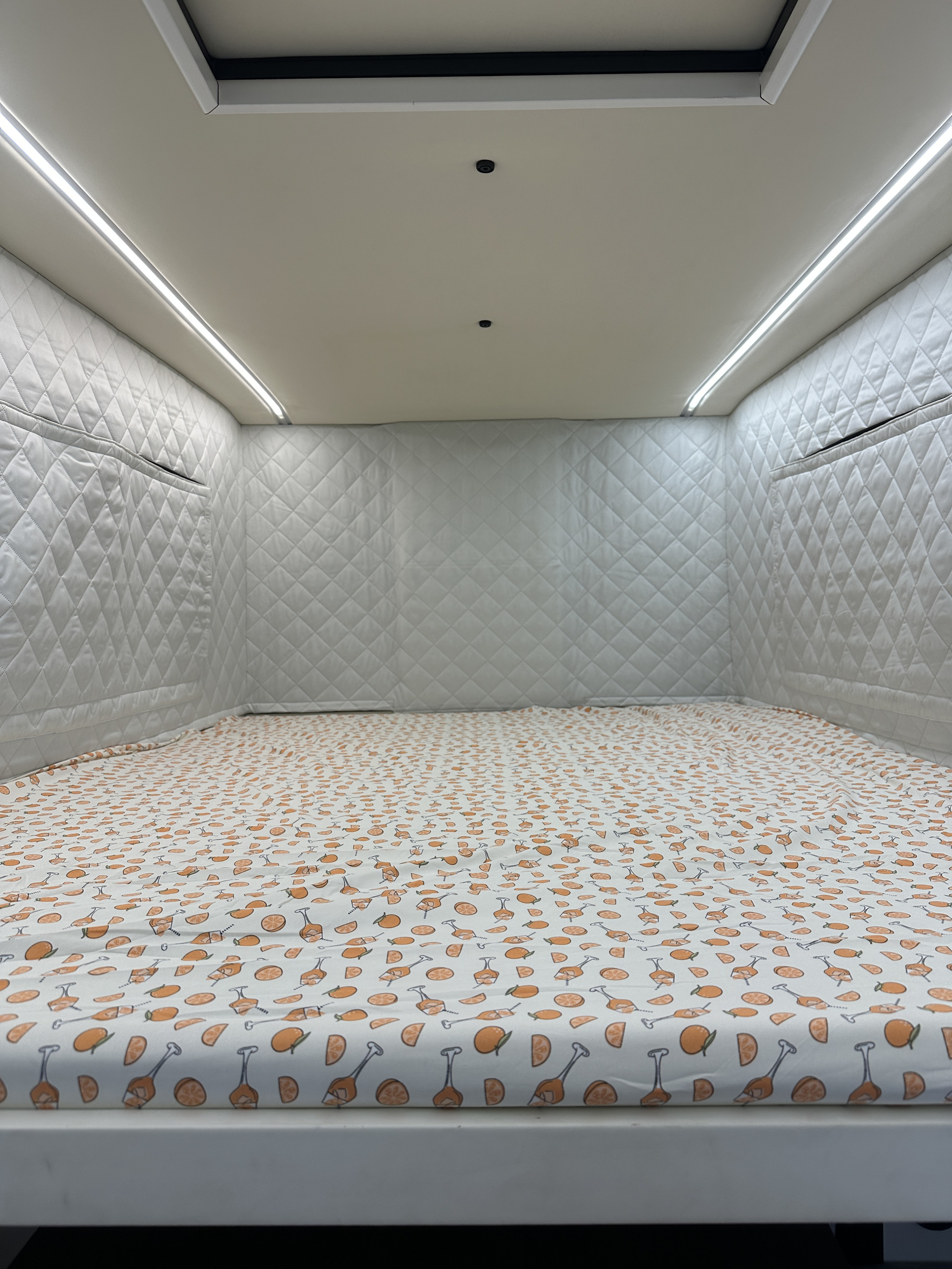 Cozy RV rental interior featuring a bed with vibrant citrus sheets, soft quilted walls, and bright ambient LED lighting.. Four Wheel Campers Toyota Tacoma 2025