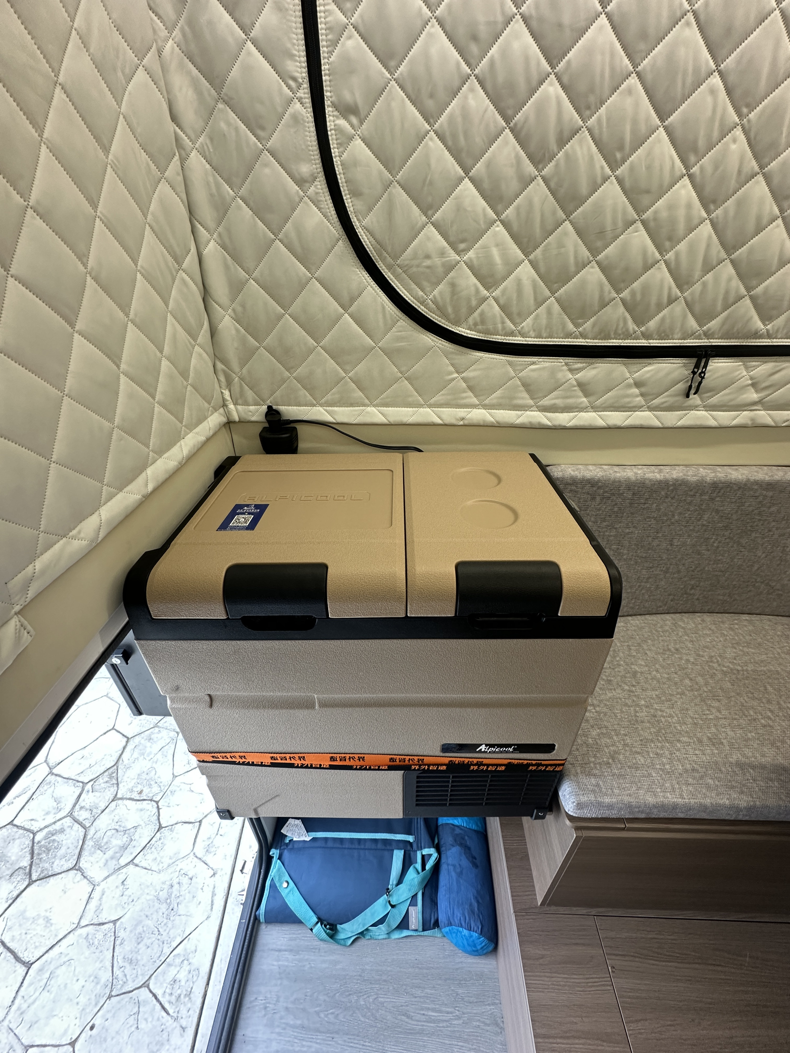 This compact RV rental interior features an Alpicool portable fridge, quilted pop-top walls, a bench, and under-storage.. Four Wheel Campers Toyota Tacoma 2025