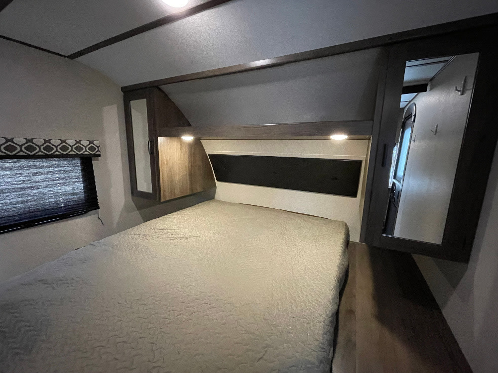 Experience comfort in this RV rental bedroom: bed with overhead cabinets, window with blind, and mirrored closet.. Forest River Tracer 2020