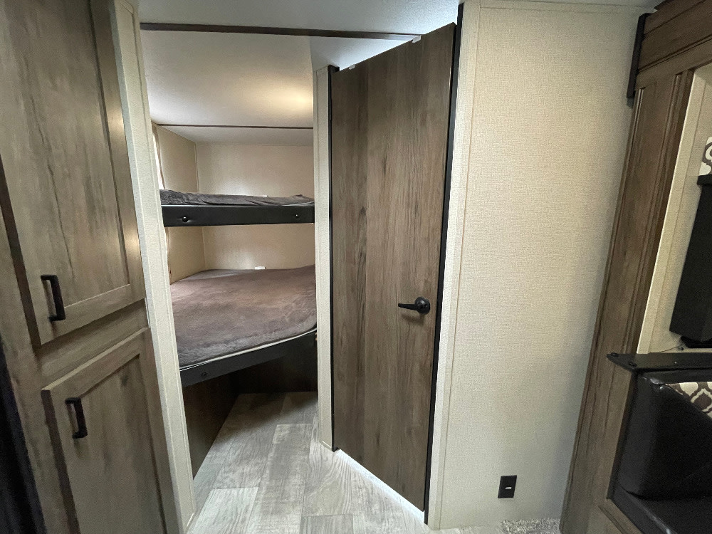 RV rental interior: cozy bunk room with two beds, a privacy door, and built-in cabinets.. Forest River Tracer 2020