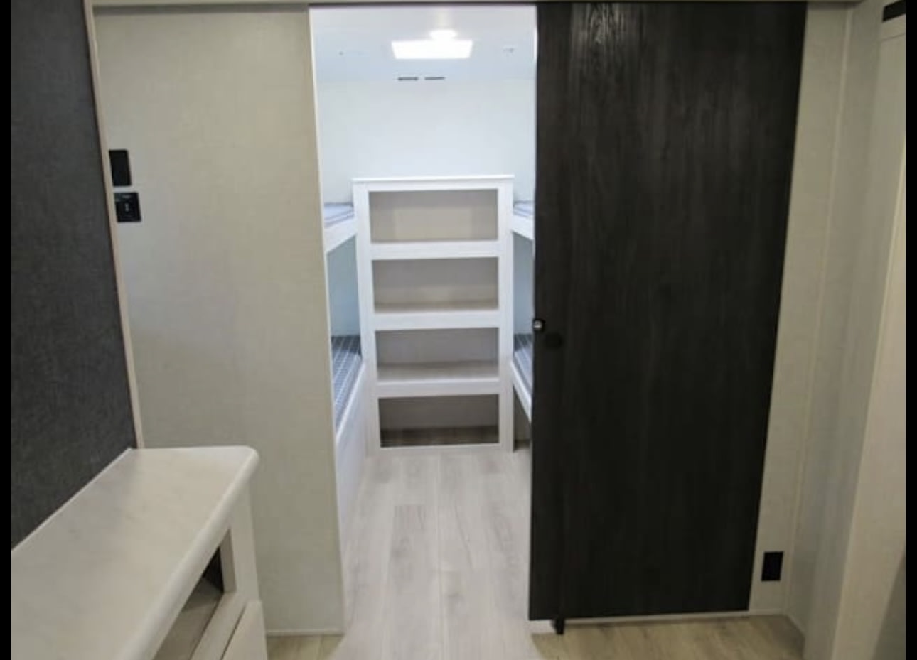 RV rental bunk room with white beds and central shelving, accessed via sliding doors.. First river Surveyor 2025