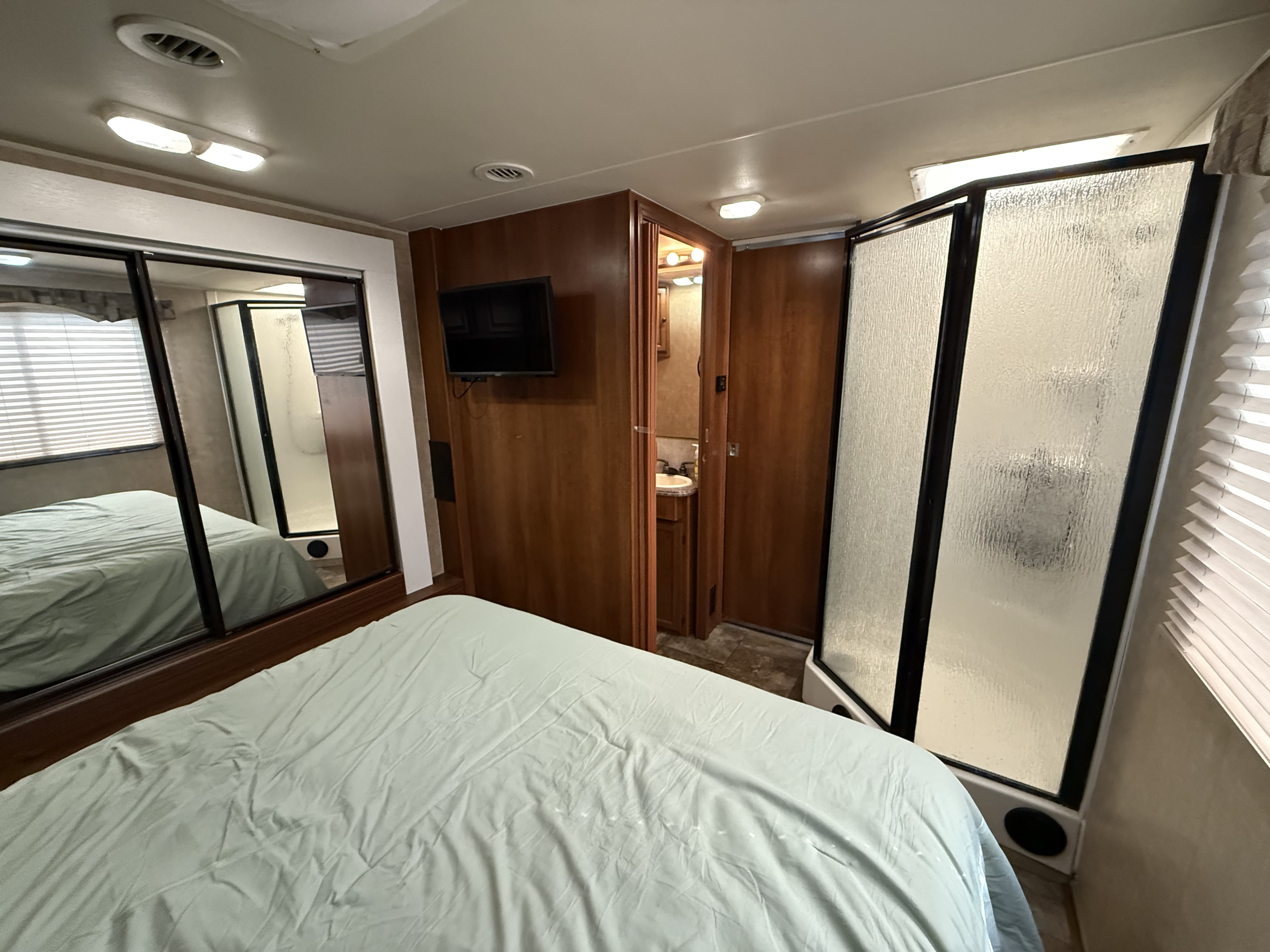 RV rental bedroom featuring a bed, mirrored closet, mounted TV, plus an accessible bathroom and separate shower stall.. Coachman Leprechaun 320 2012