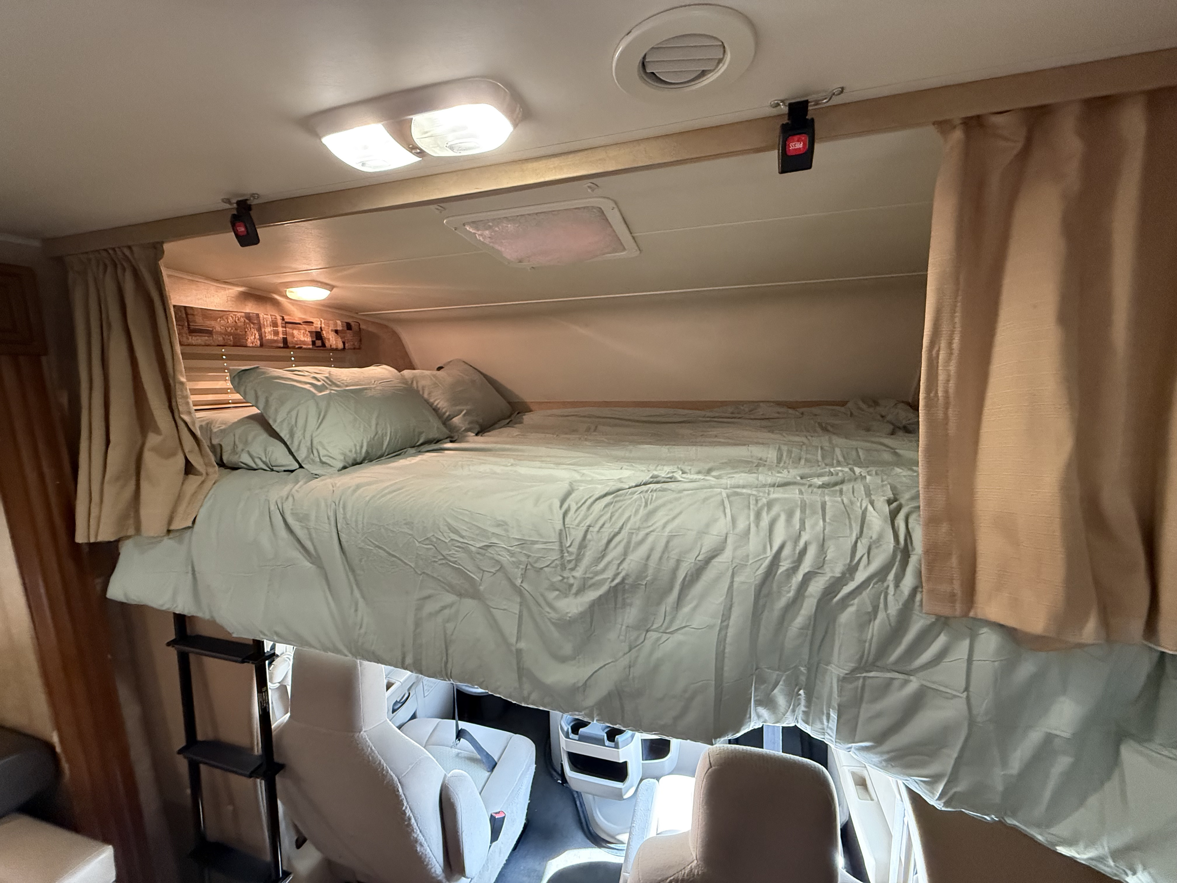 This RV rental's cab-over bunk features a sage green bed, access ladder, privacy curtains, and safety strap buckles.. Coachman Leprechaun 320 2012