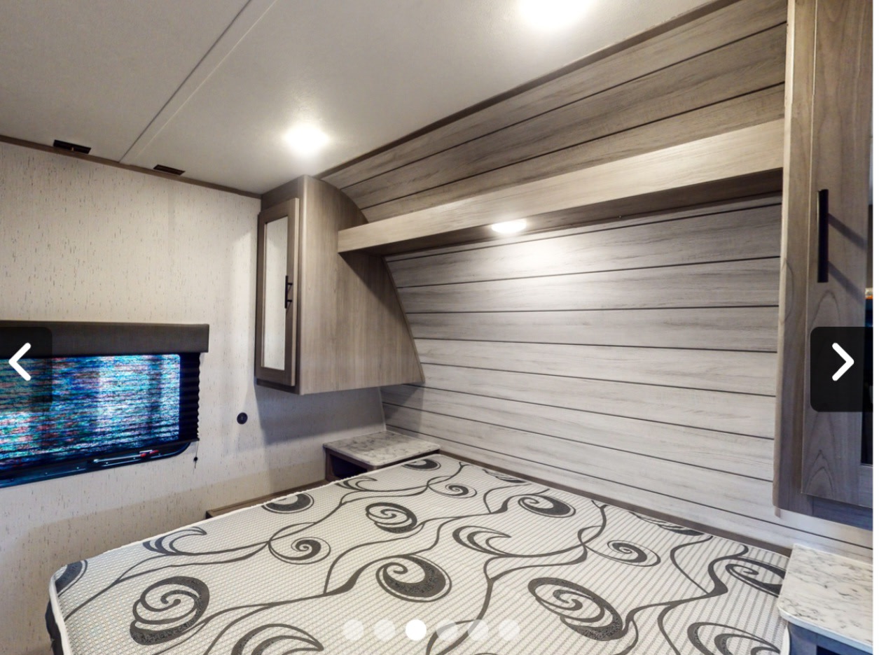 Inside an RV rental, this cozy bedroom features a patterned bed, wood-paneled walls, and convenient overhead storage.. Coleman Lt274bh 2024