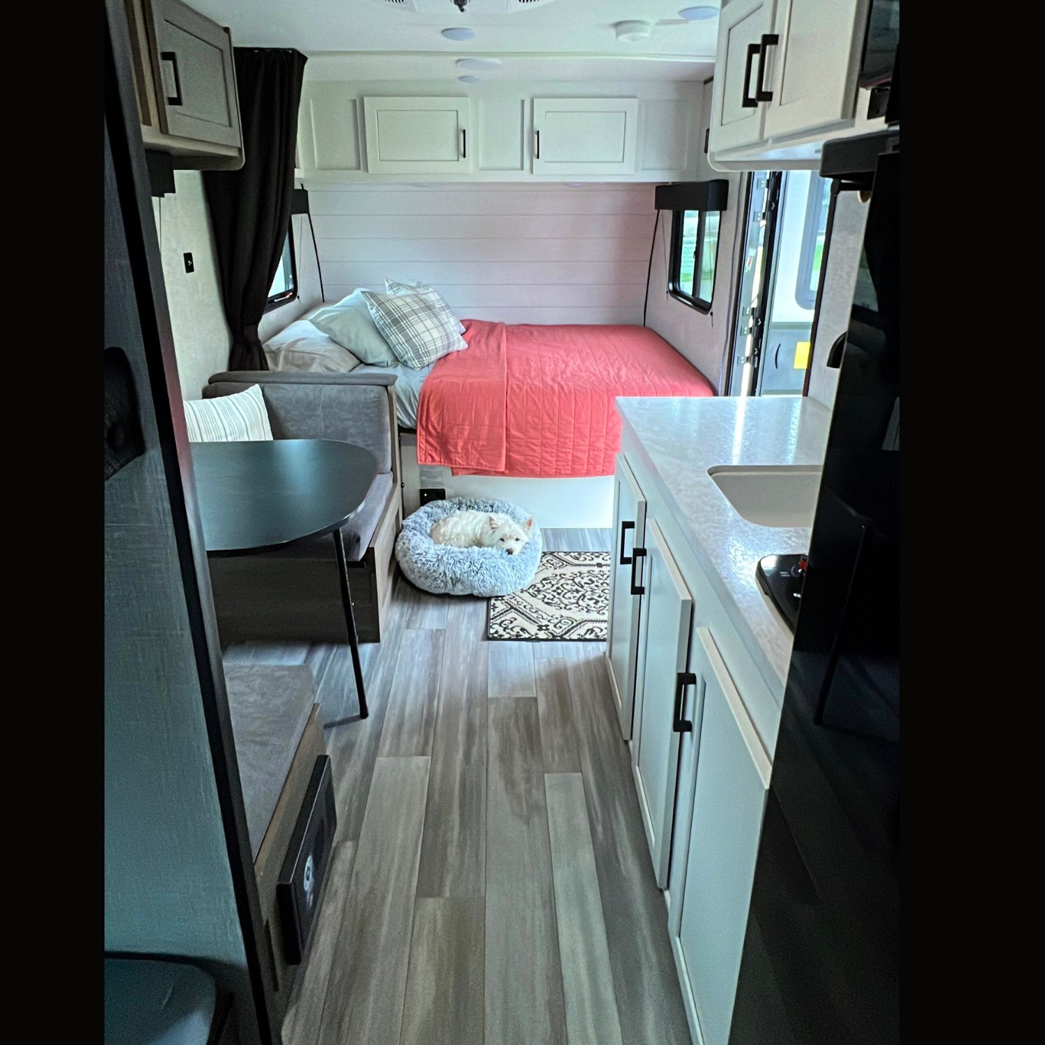 Inside a cozy RV rental: kitchen counter, bed with red comforter, dinette, and a sleeping dog. Great camper amenities.. Jayco Jay Flight SLX Baja Edition 2024