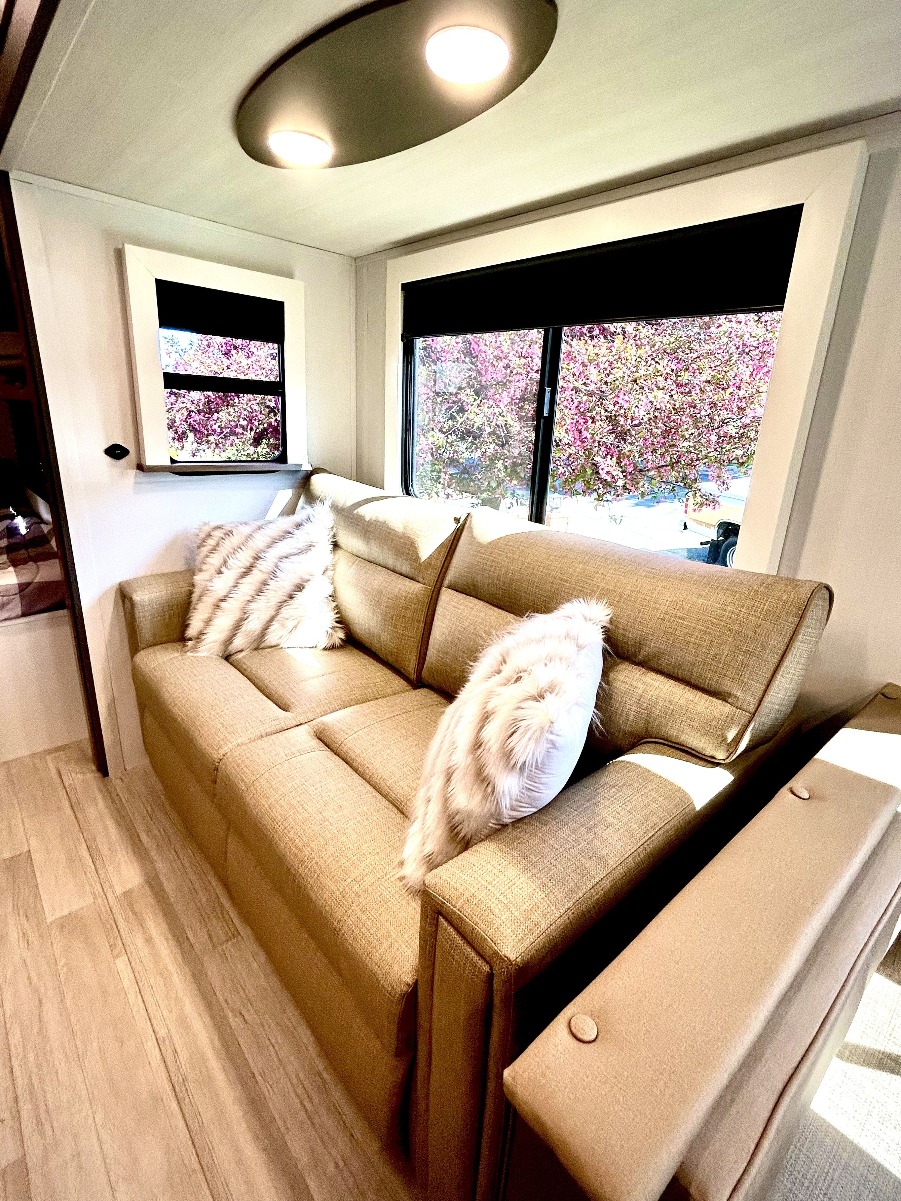 Bright RV rental interior with a comfy sofa, fluffy pillows, and large windows showing a blooming tree outside.. Keystone Rv 290BHSWE 2025