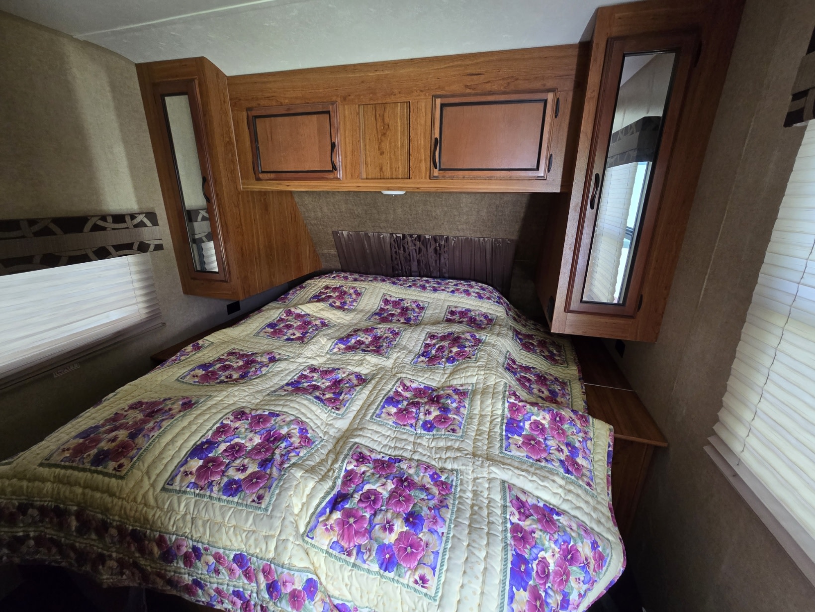 Step into comfort! This RV rental bedroom features a floral quilt, wooden cabinets, and convenient bedside storage.. Starcraft Autumn Ridge 2017