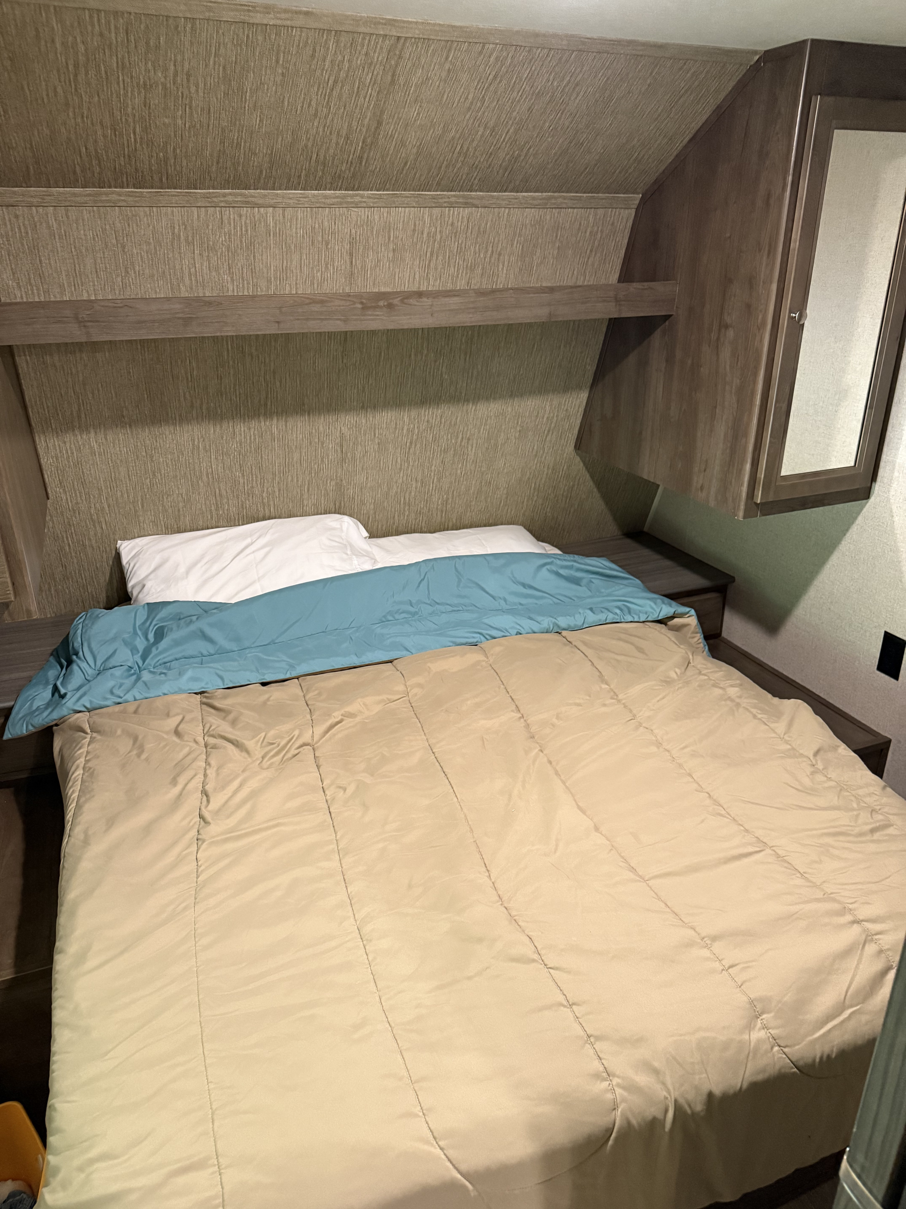 RV rental bedroom interior, featuring a bed, shelf, and storage cabinet.. Dutchmen Coleman Lantern 2019