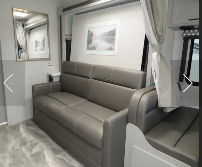 Inside a modern RV rental: a grey sofa-bed, stylish wall art, and mirrored wall. Ideal for travel comfort.. Thor Quantum LC 2022