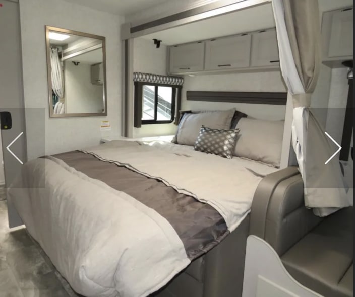 Cozy RV rental bedroom featuring a large bed with neutral bedding, overhead cabinets, and a comfortable living space.. Thor Quantum LC 2022