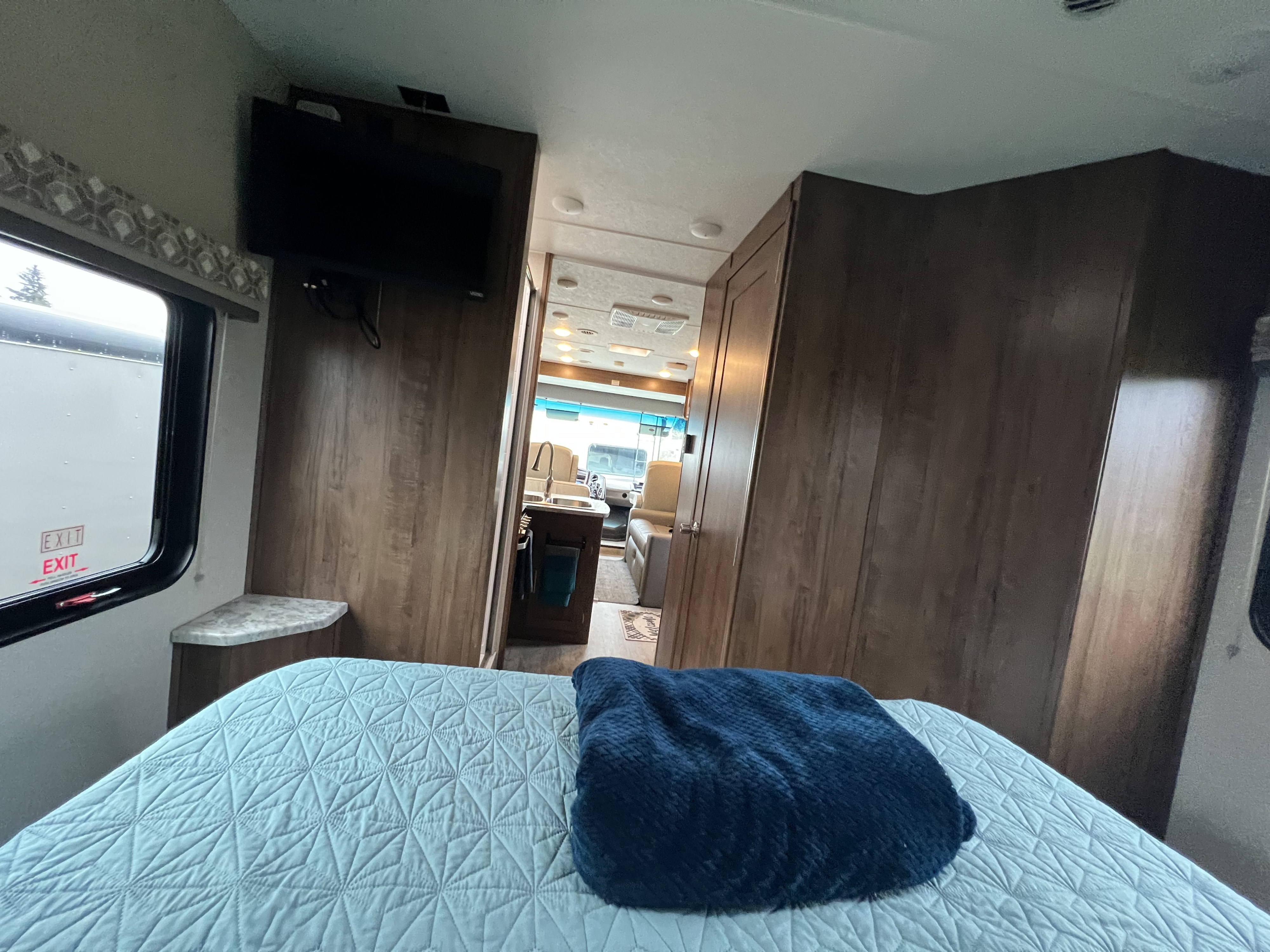 Inside an RV rental: Cozy bedroom featuring a bed, TV, and a view into the kitchen and living area.. Coachman RV Pursuit 27 XPS 2020