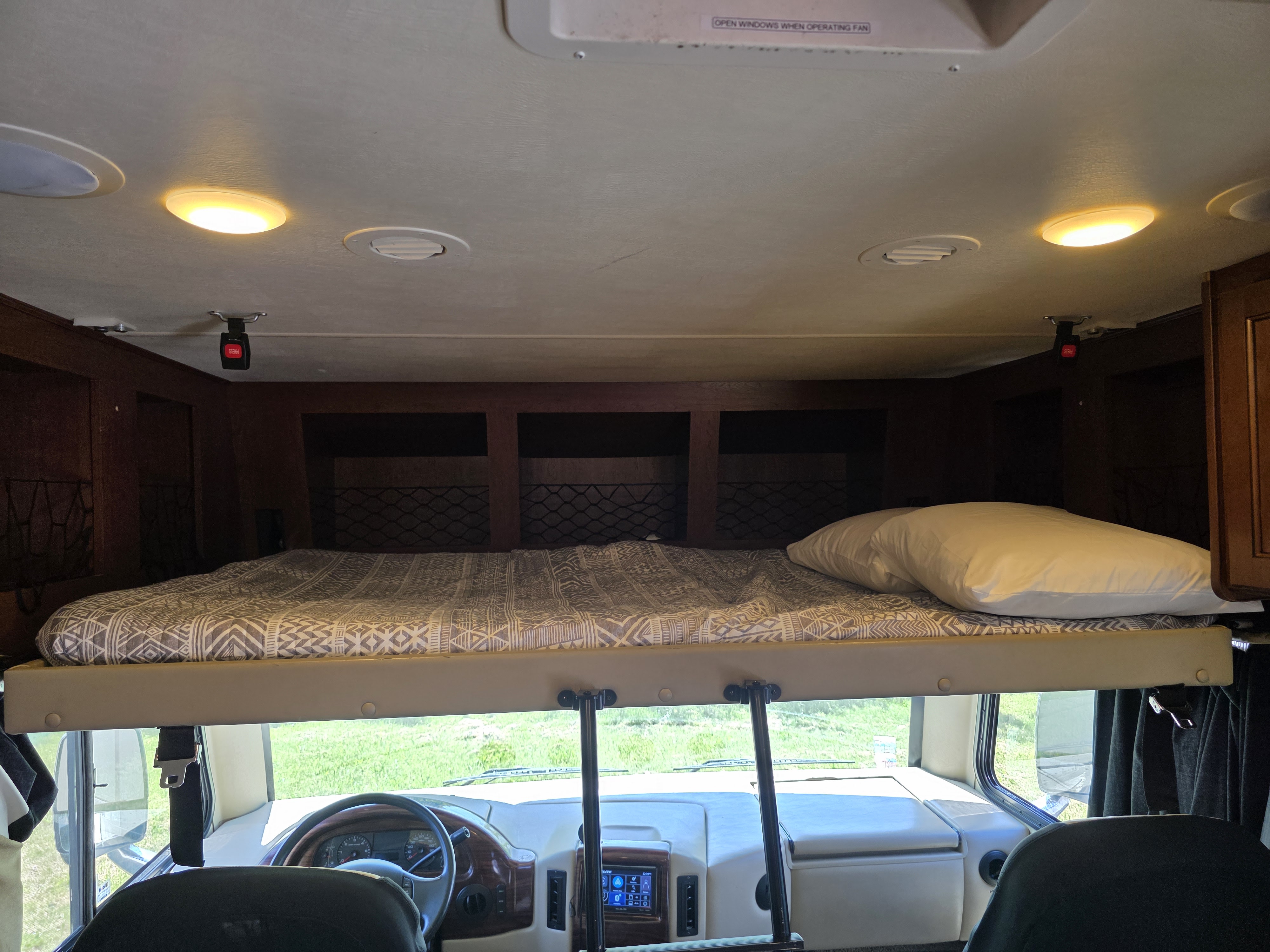 Inside an RV rental, showing the comfy overhead bunk bed above the driver's cockpit and windshield view of outdoors.. Thor Motor Coach A.C.E 2017