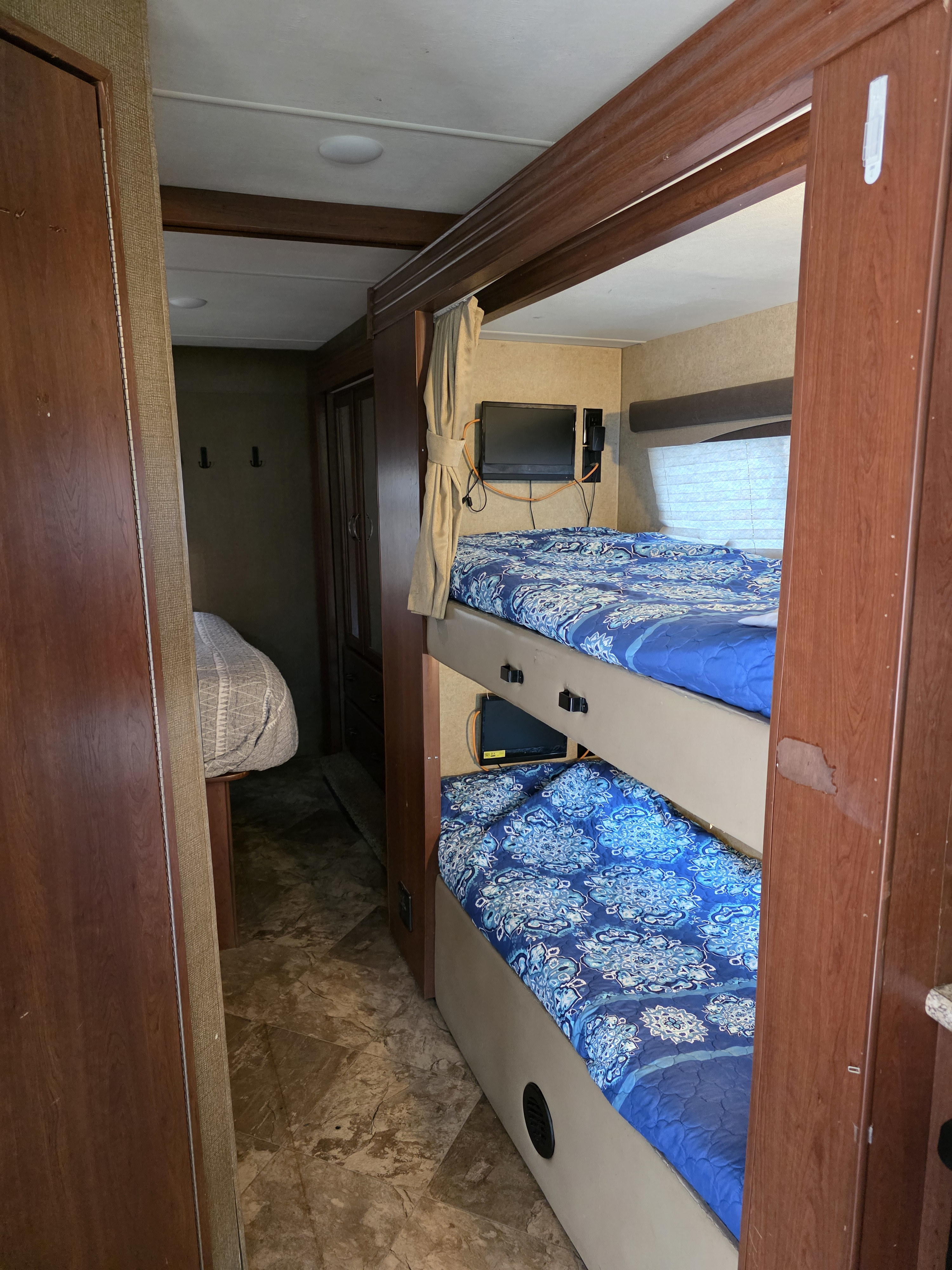 Inside an RV rental: blue-patterned bunk beds with TV, leading to another bedroom with a grey bed. Compact & cozy.. Thor Motor Coach A.C.E 2017