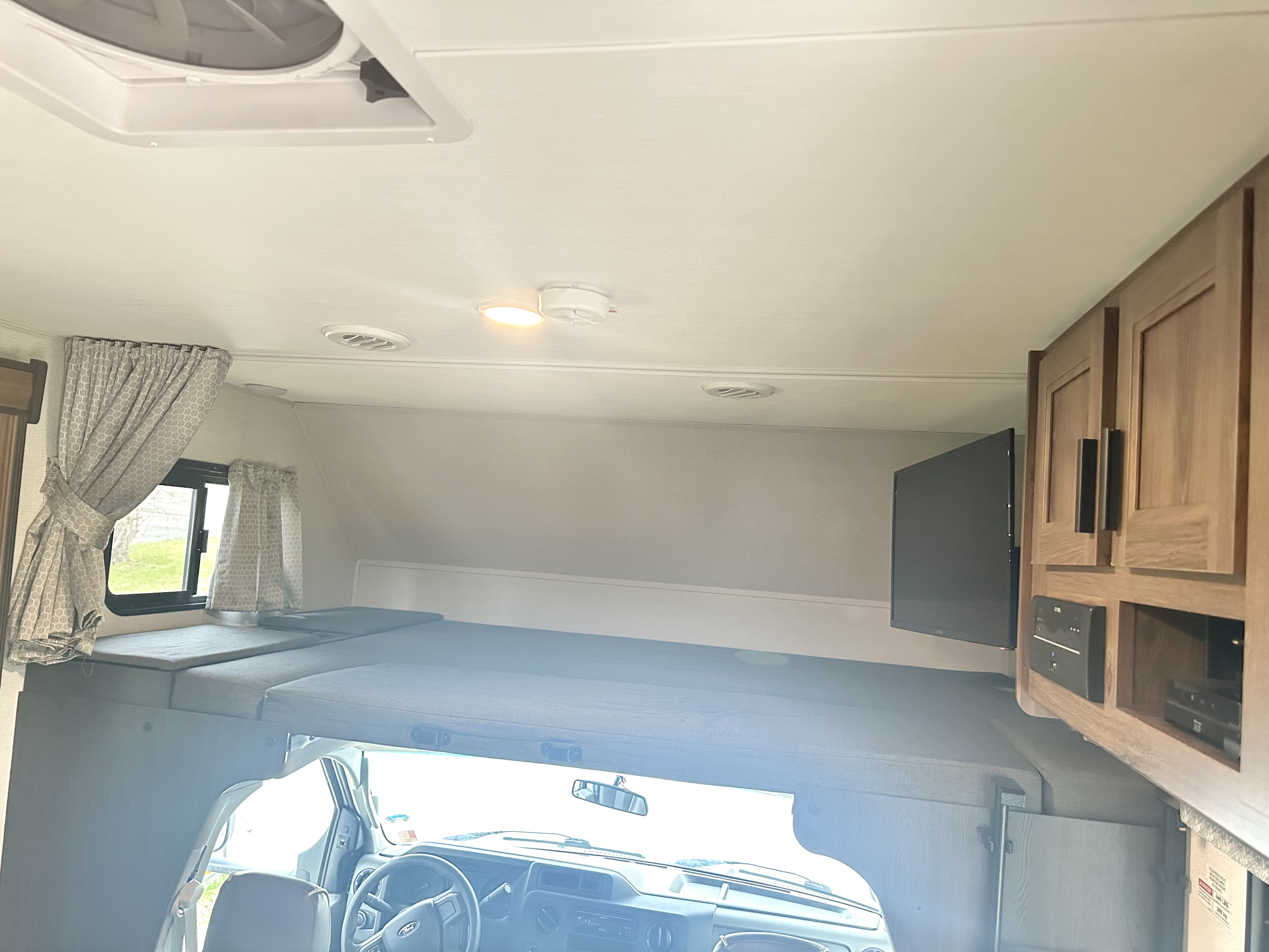 Spacious RV rental interior with cab-over bunk, driver's cockpit, ceiling vents, light, smoke detector, and entertainment TV.. Forester LE 2022