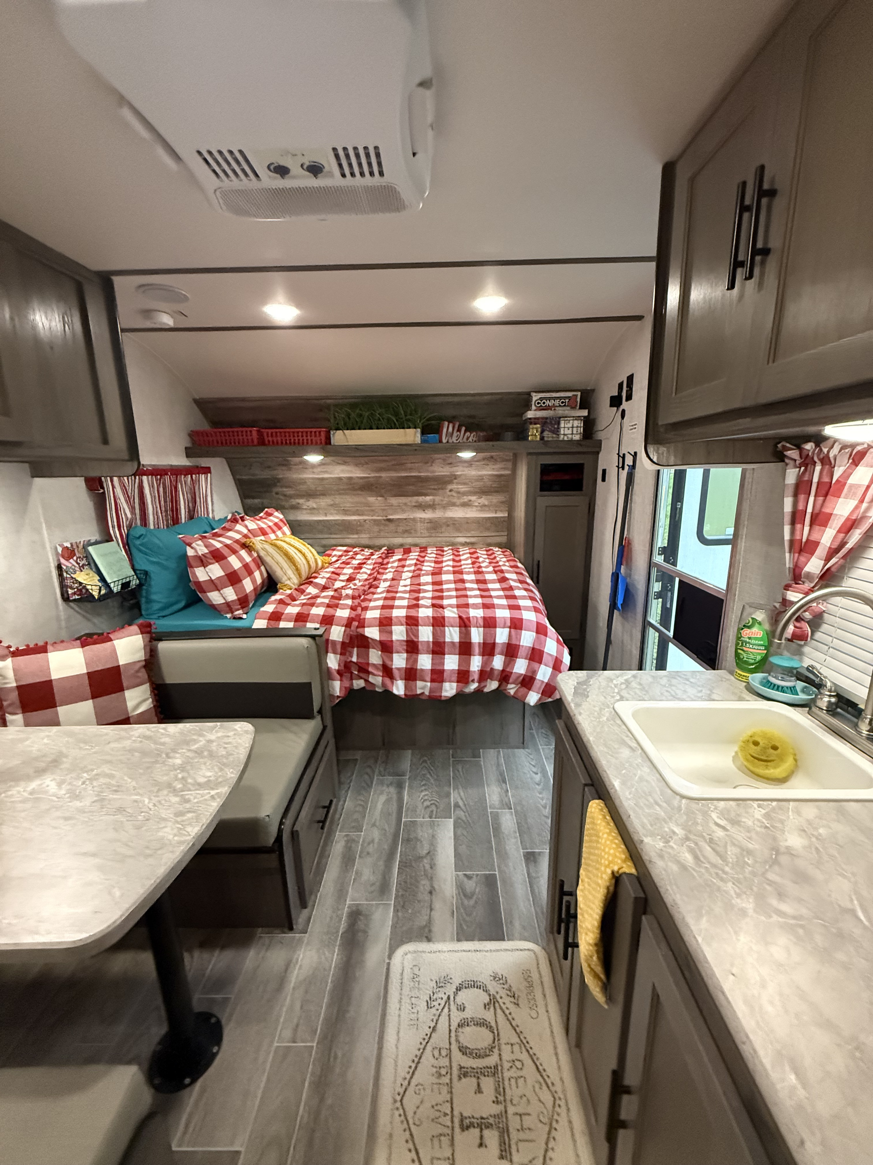 Cozy RV rental interior featuring a checkered bed, dinette, and kitchen sink, ideal for travel.. Gulf Stream Ameri-Lite Super Lite 2021