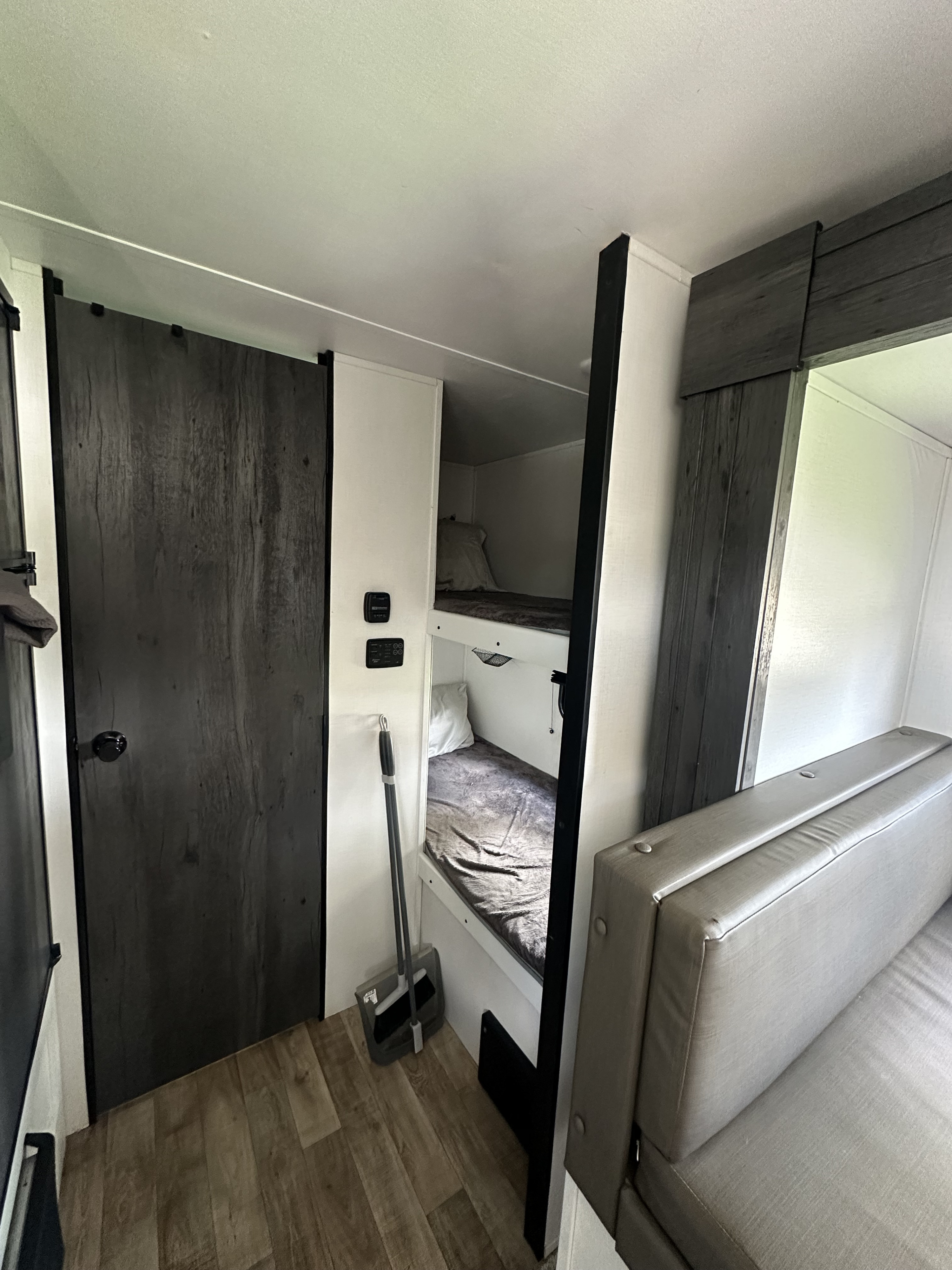 RV rental interior featuring a modern dark wood door, bunk beds, and a gray seating area in a compact, functional space.. Keystone RV Hideout 2022