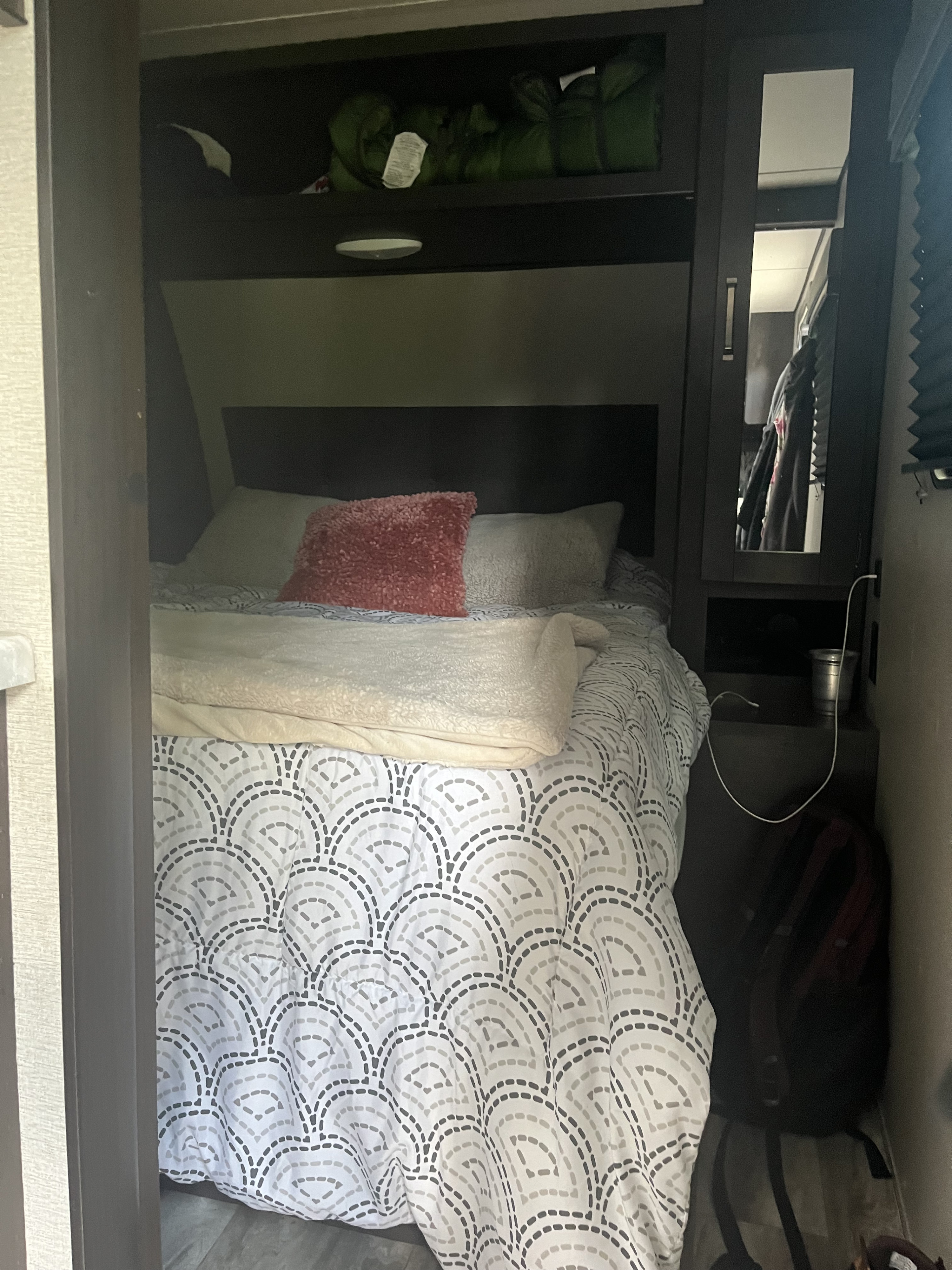 This RV rental features a cozy bedroom with patterned bedding, convenient overhead storage, and a mirrored cabinet.. Grand Design Transcend Xplor 2021