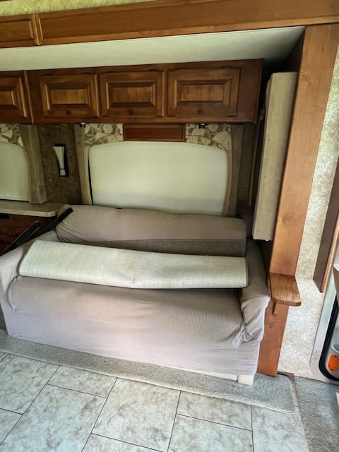 RV rental interior featuring a convertible sofa bed, overhead cabinets, and a window, ideal for mobile living.. Allegro Tiffin Allegro Open Road 2012