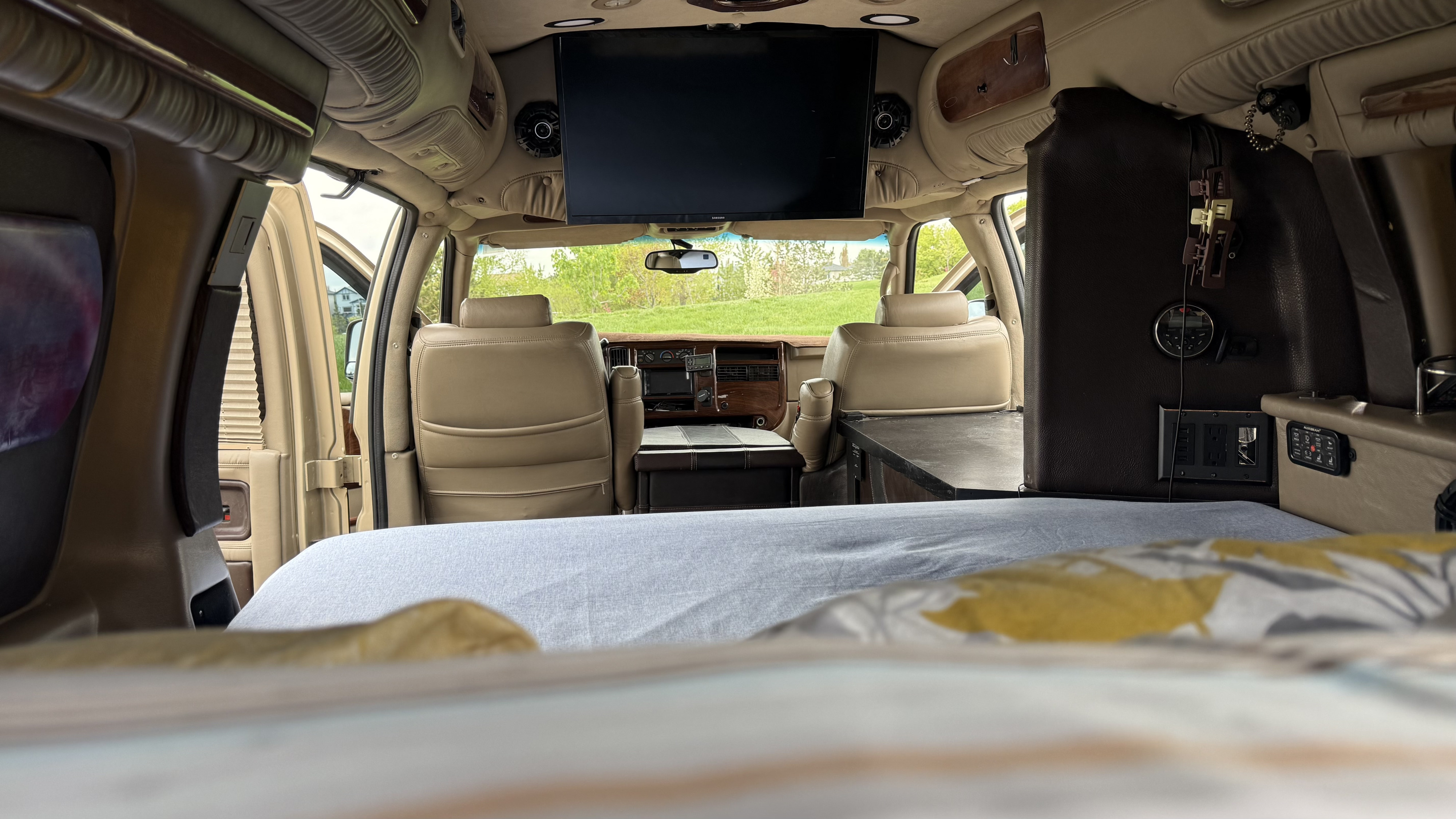 Inside an RV rental: Looking forward from the bed, revealing tan front seats, an overhead TV, and utility controls.. Gmc Custom Savana 2007