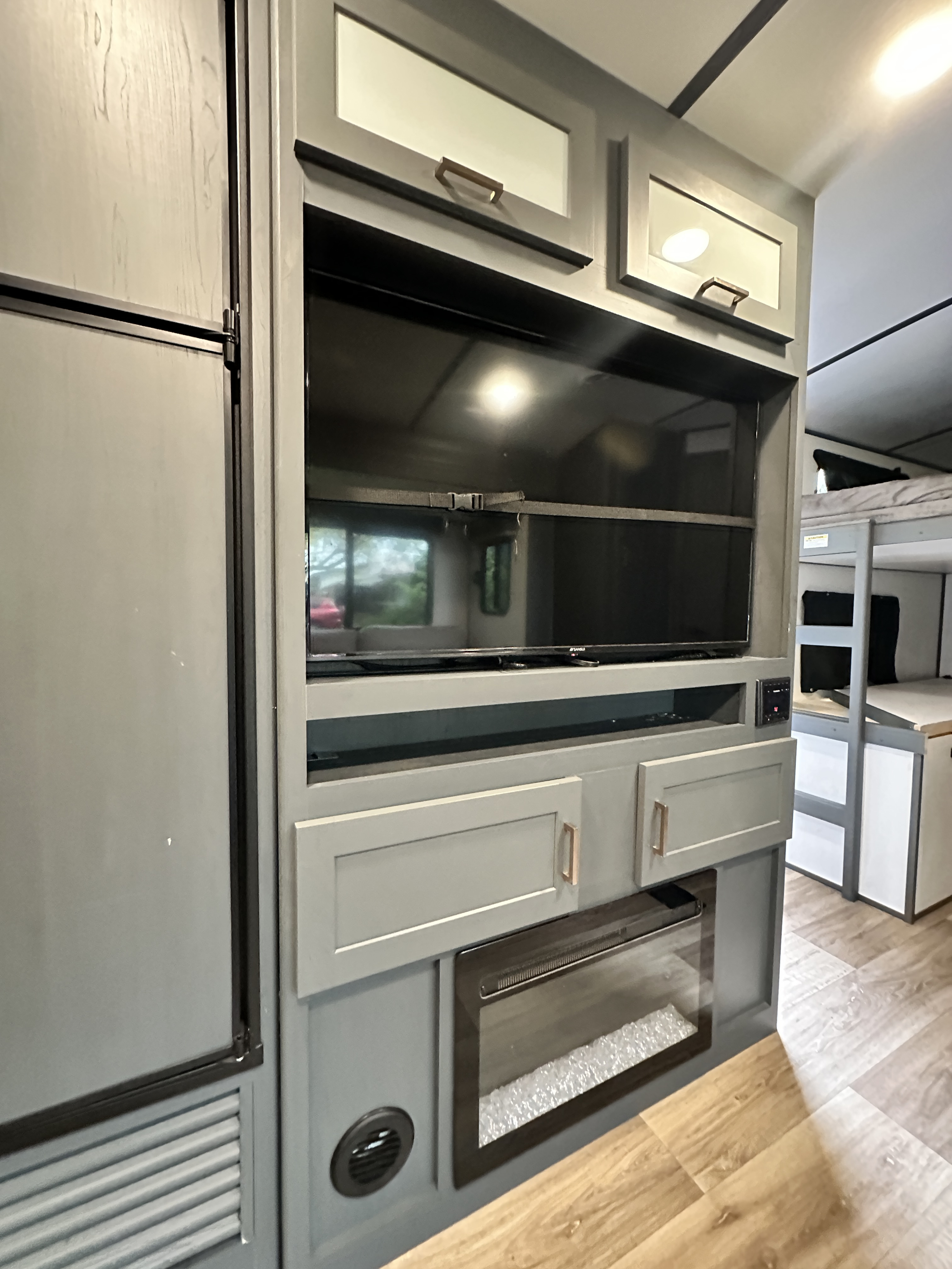 Modern grey RV rental interior featuring an entertainment center with a TV, electric fireplace, and adjacent refrigerator. Bunk beds are visible.. Keystone Premier 29BHPR 2022