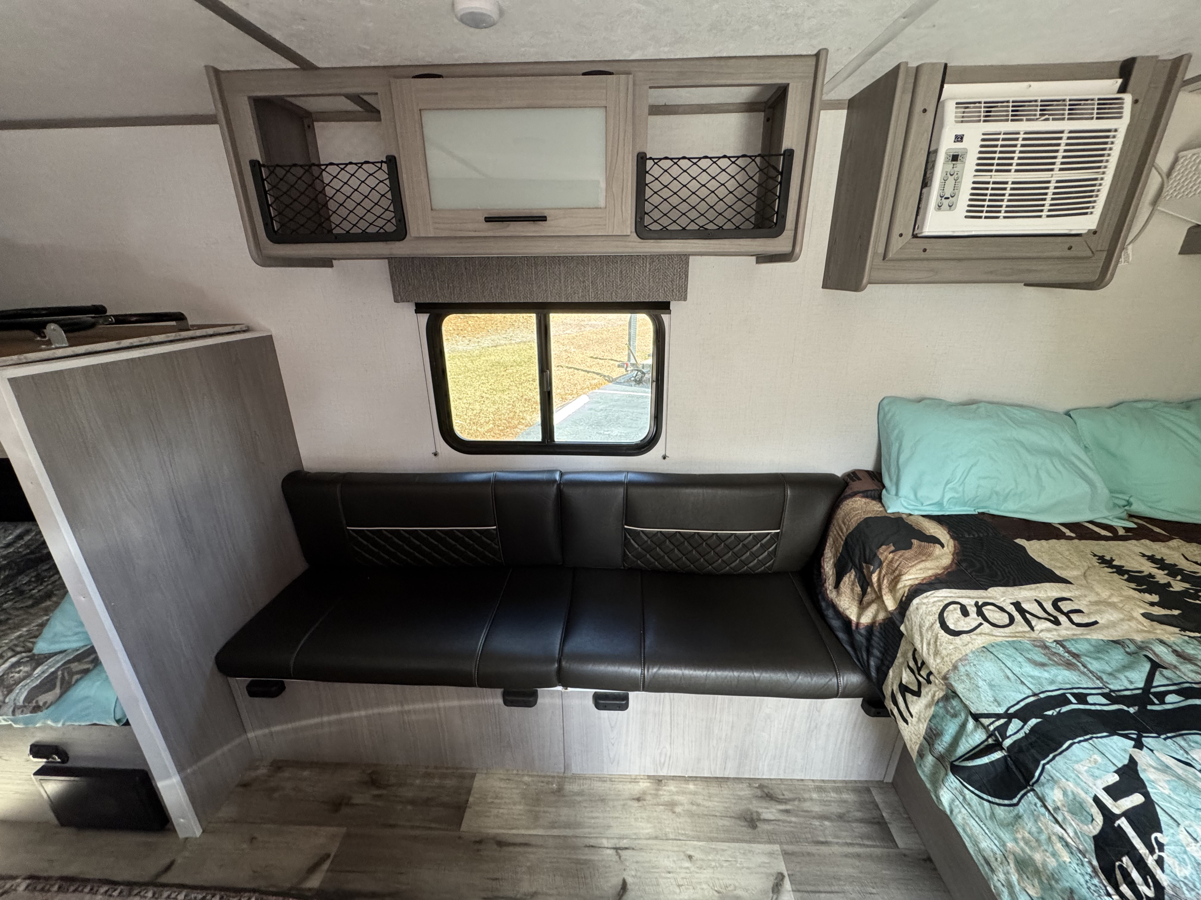 RV rental interior showcasing a black leather sofa, window, overhead cabinets, air conditioner, and bed.. Keystone RV Coleman Lantern 17B 2024