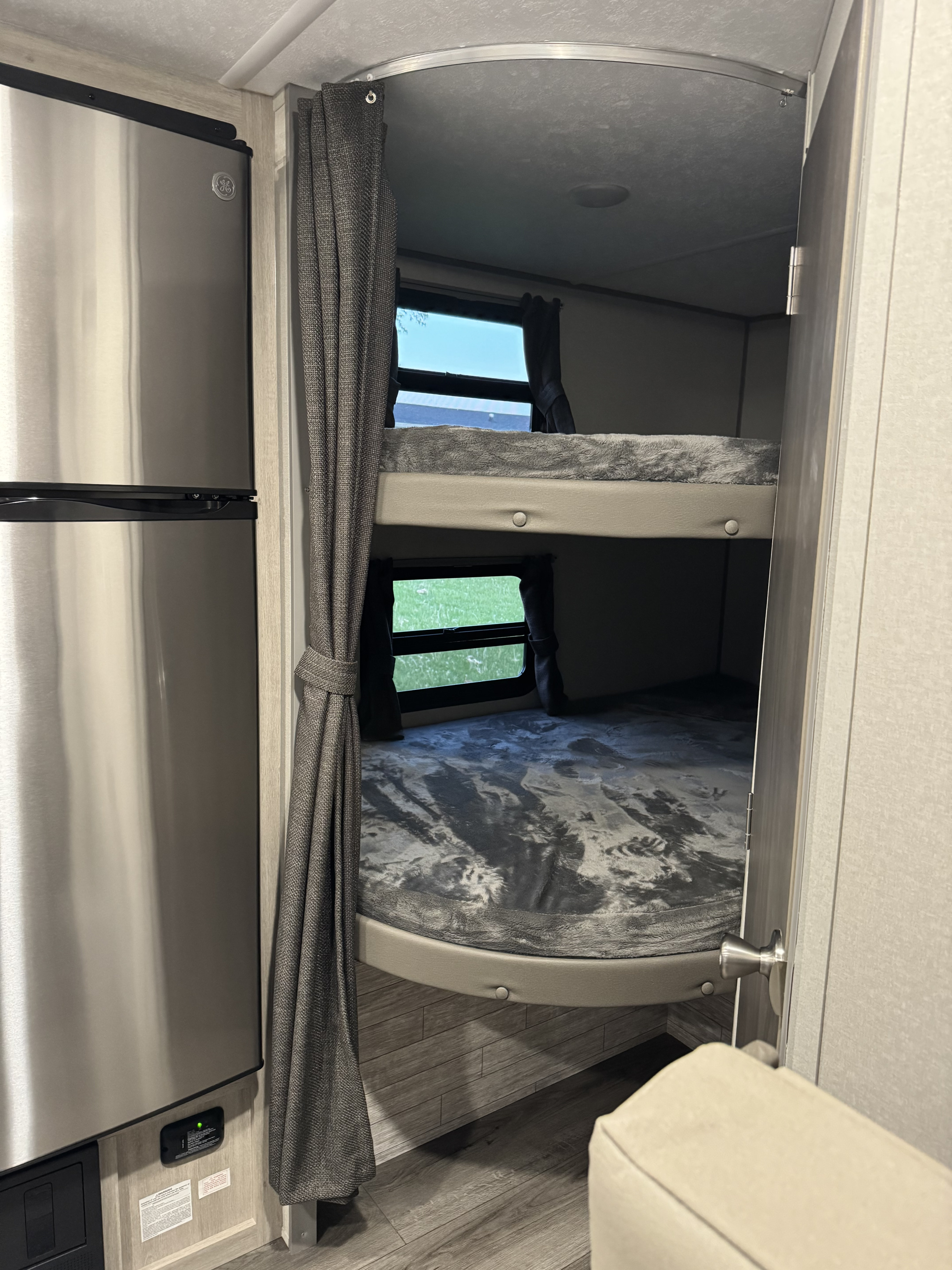 Compact RV rental interior: stainless steel fridge, two bunk beds with windows and curtains.. Forest River 184BHS 2025