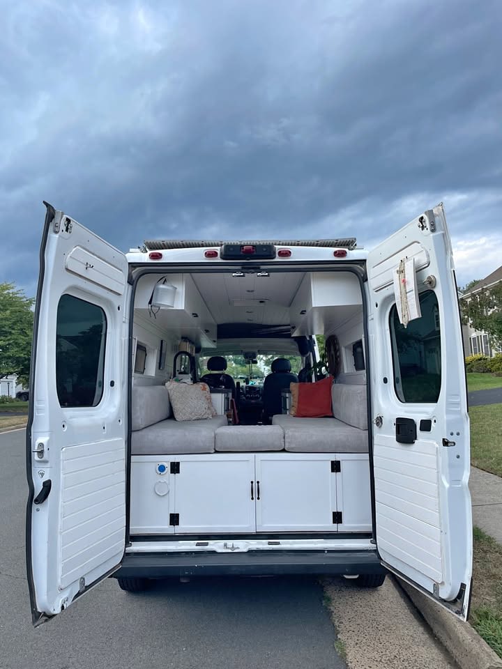 Explore this modern RV rental camper van conversion, with open rear doors showcasing its cozy seating/bed and storage.. Ram Ram ProMaster 2500 2019