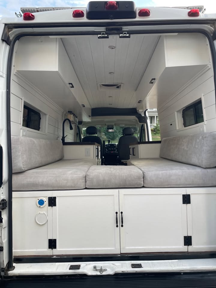 RV rental: Rear view inside a white camper van conversion with a gray cushioned bed, built-in cabinets, and sink.. Ram Ram ProMaster 2500 2019