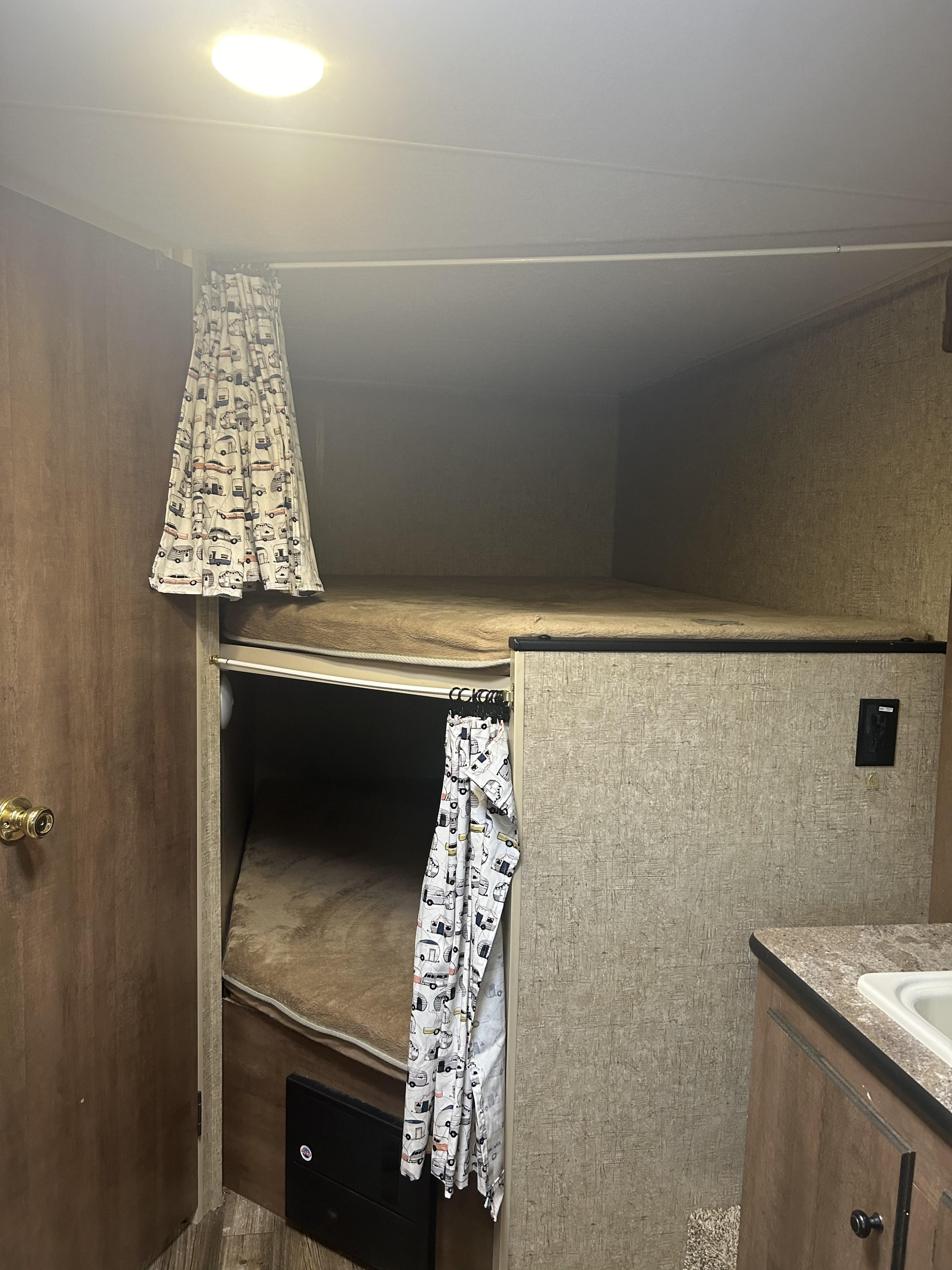 RV rental: Brightly lit interior shows comfortable bunk beds with playful camper-print curtains.. KZ Escape 2017