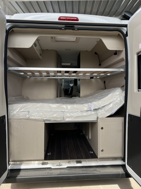 Inside an RV rental: a spacious rear area with a bed, an upper bunk frame, and convenient storage below.. Horus2 145 2025