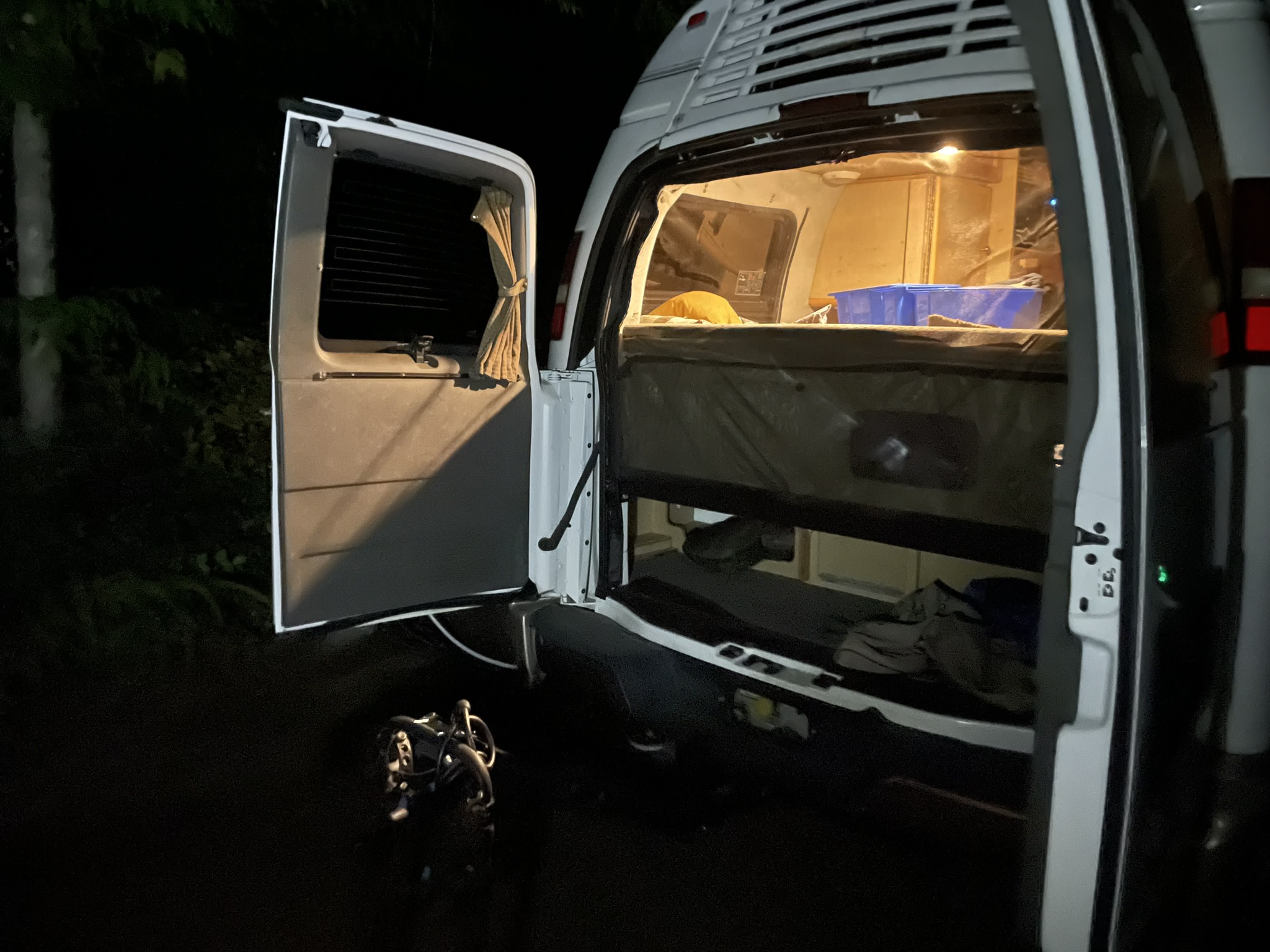 Nighttime view of an open RV rental's rear, showing its cozy, lit interior with a bed and storage. Ideal for road trips!. Roadtrek 210 - Popular 2005