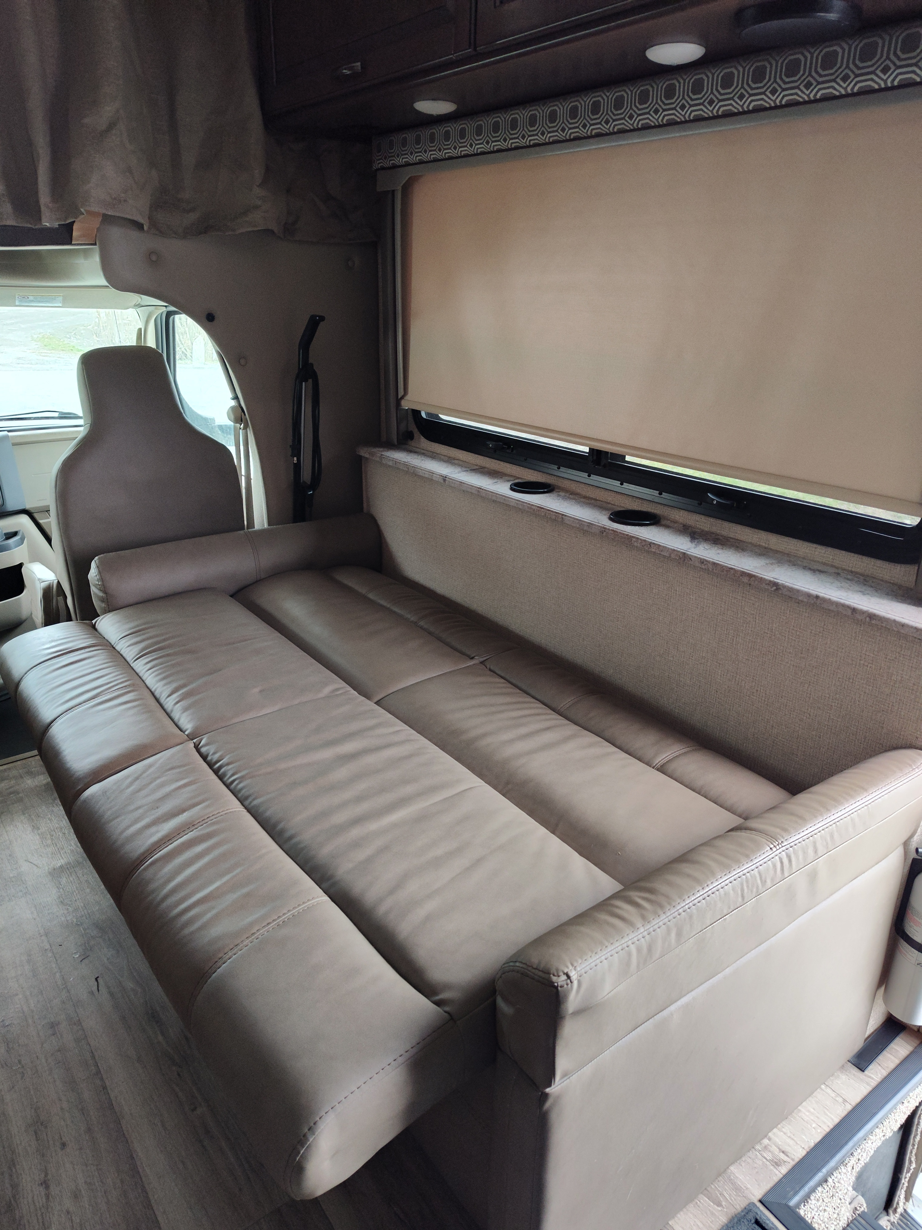 Spacious tan convertible sofa bed in an rv rental's interior, showing window, wood floor, and driver's cabin.. Thor Four Winds 2018