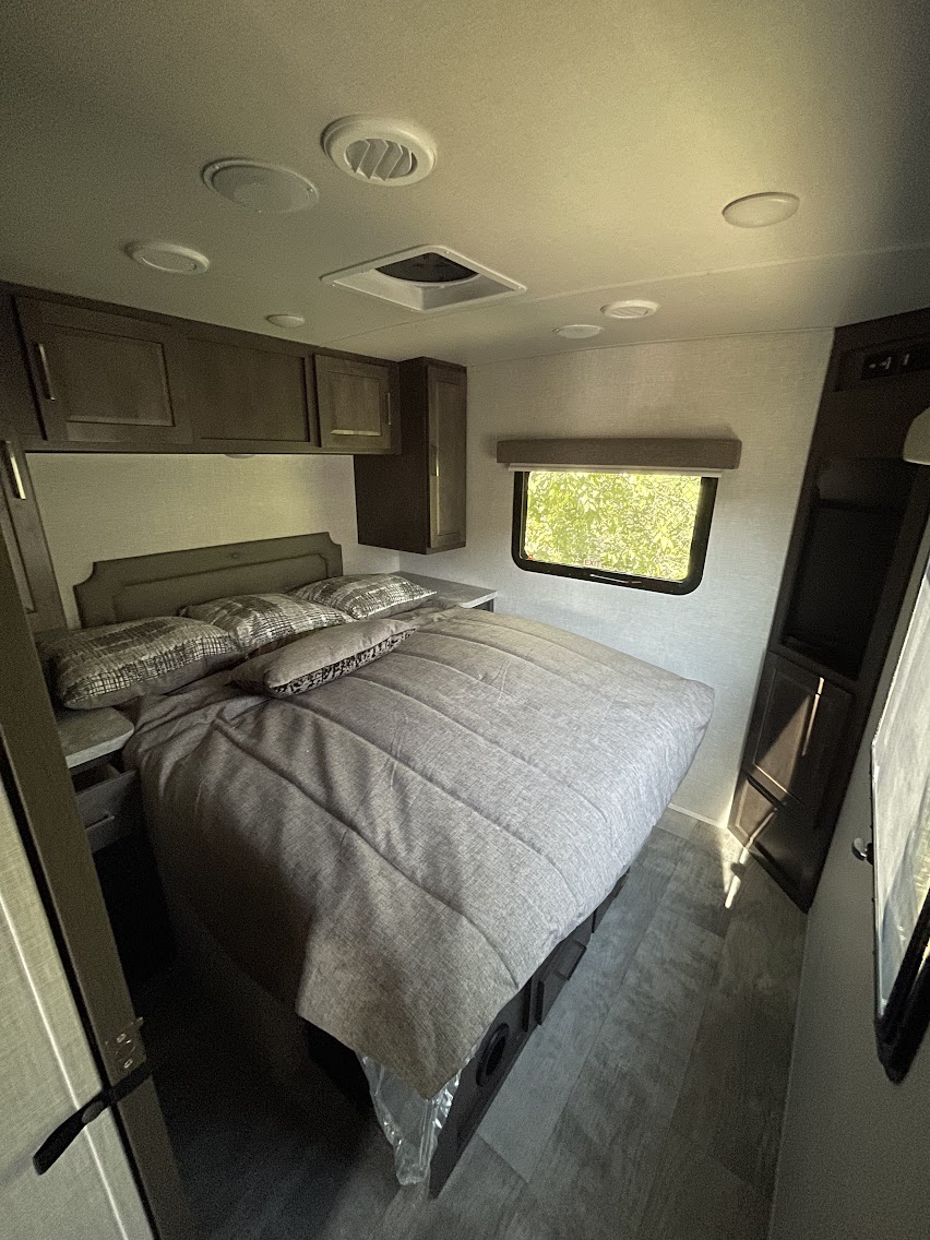 Comfortable RV rental bedroom with a cozy bed, overhead cabinets, and bright window. Perfect for your next adventure.. Rockwood Lite 2021