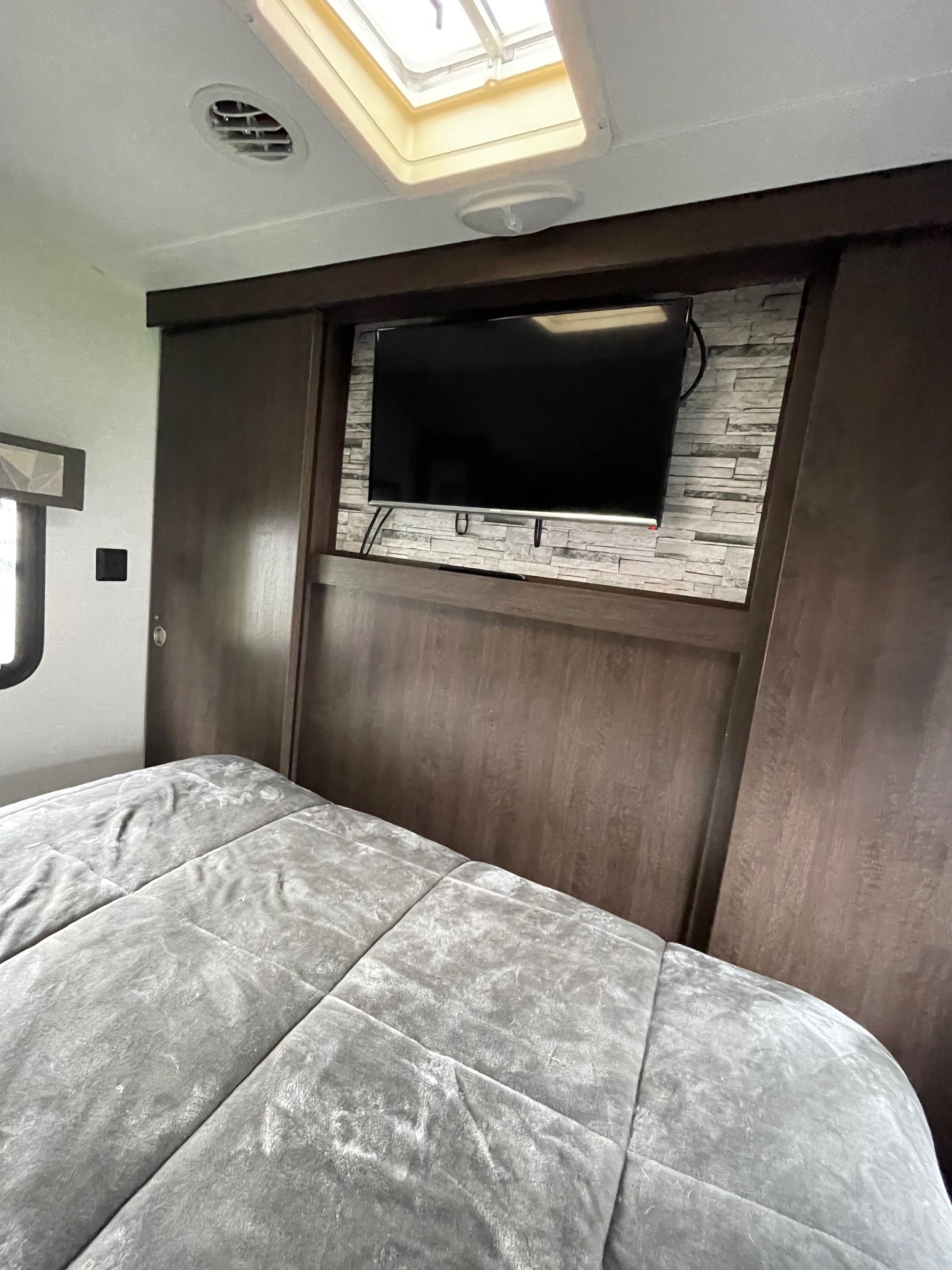 RV rental bedroom with mounted TV on a stone wall, comfortable bed, and overhead skylight.. Forest River Salem Cruise Lite 2020