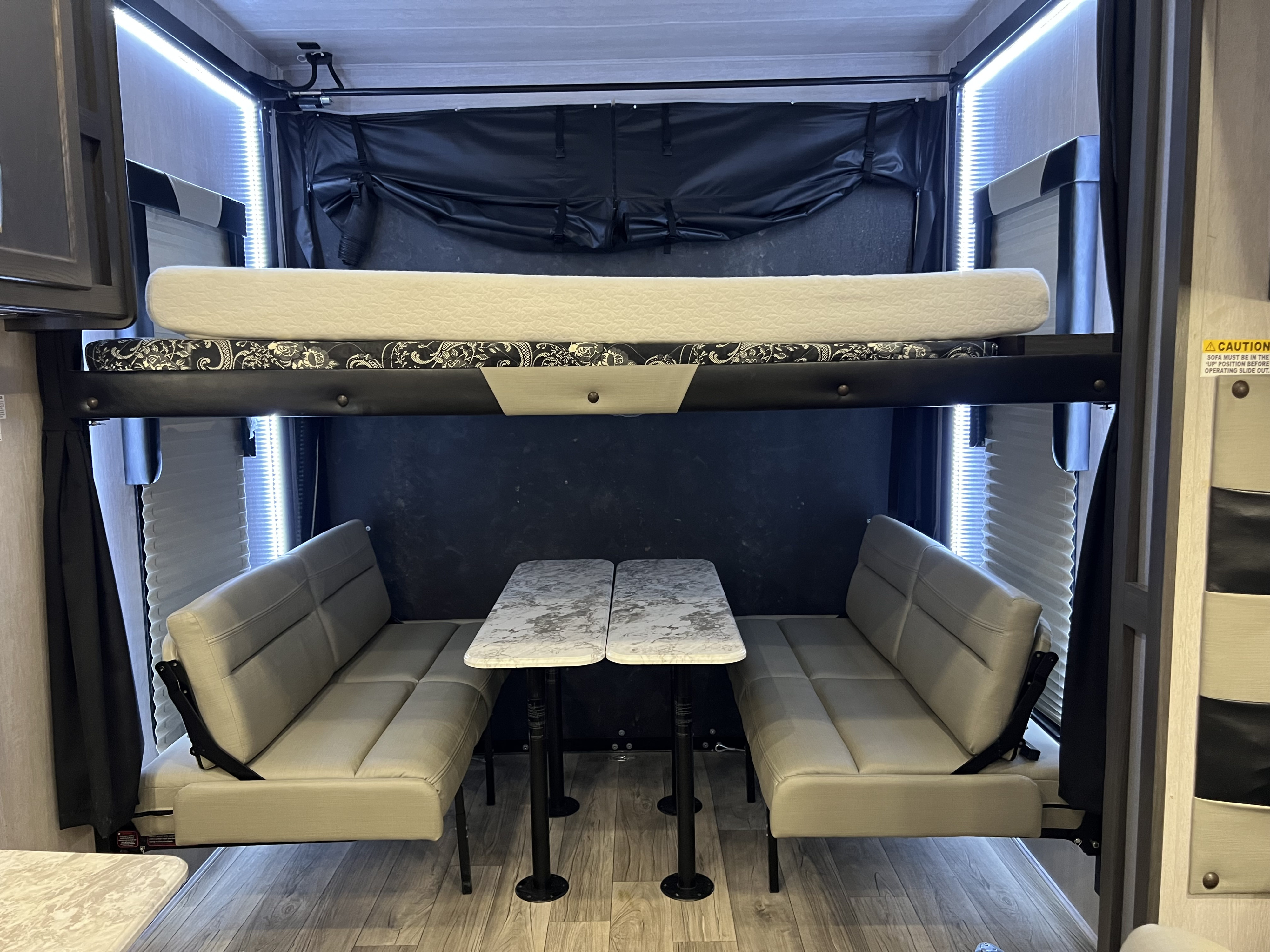 An RV rental's versatile garage space: upper bunk, lower convertible sofas, and dining table. LED lit for comfort.. Genesis Supreme 2023