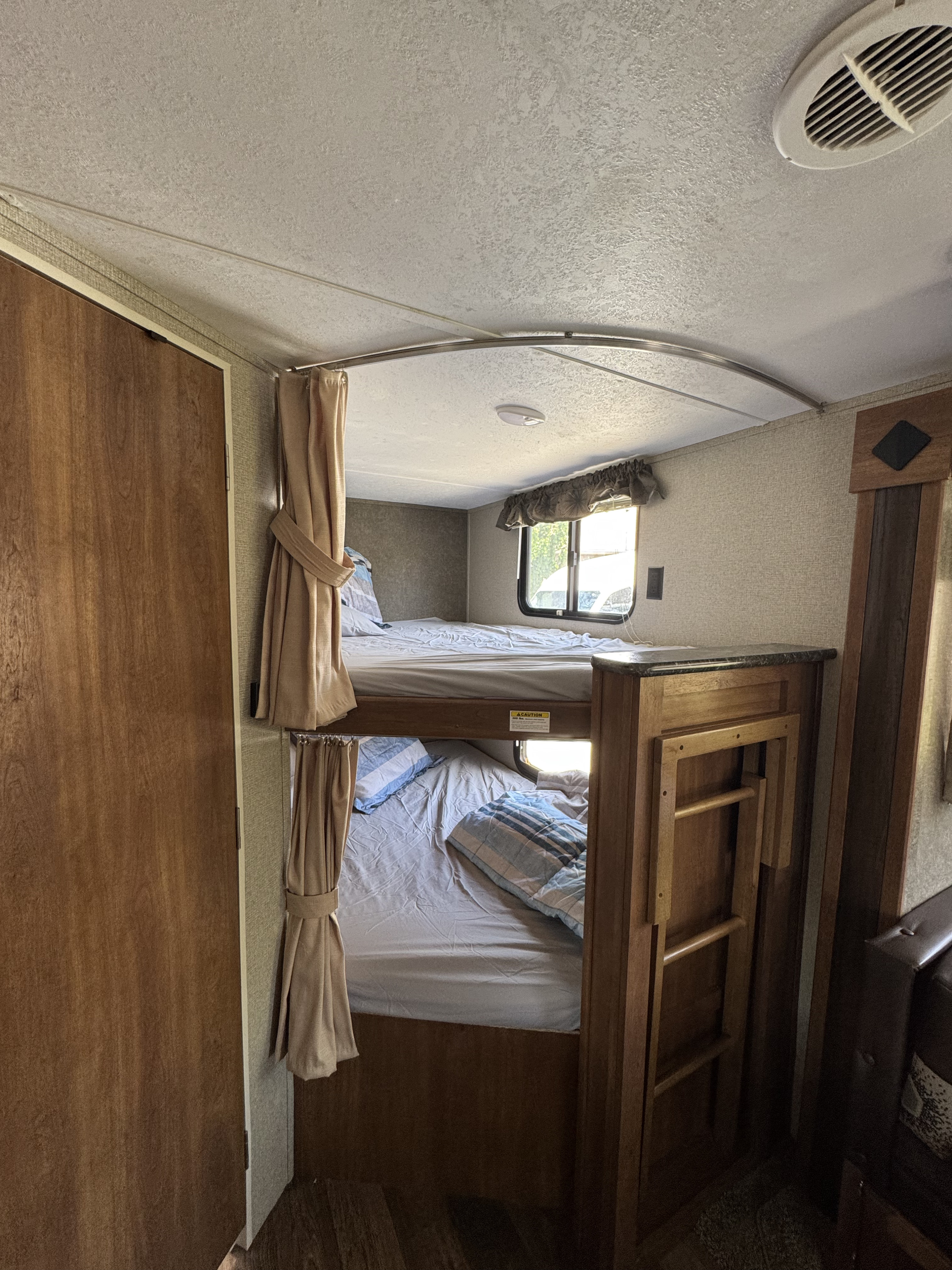 Inside an RV rental: a cozy sleeping area featuring two bunk beds with light bedding, a window, and a stored ladder.. Keystone RV Springdale SSR 2018