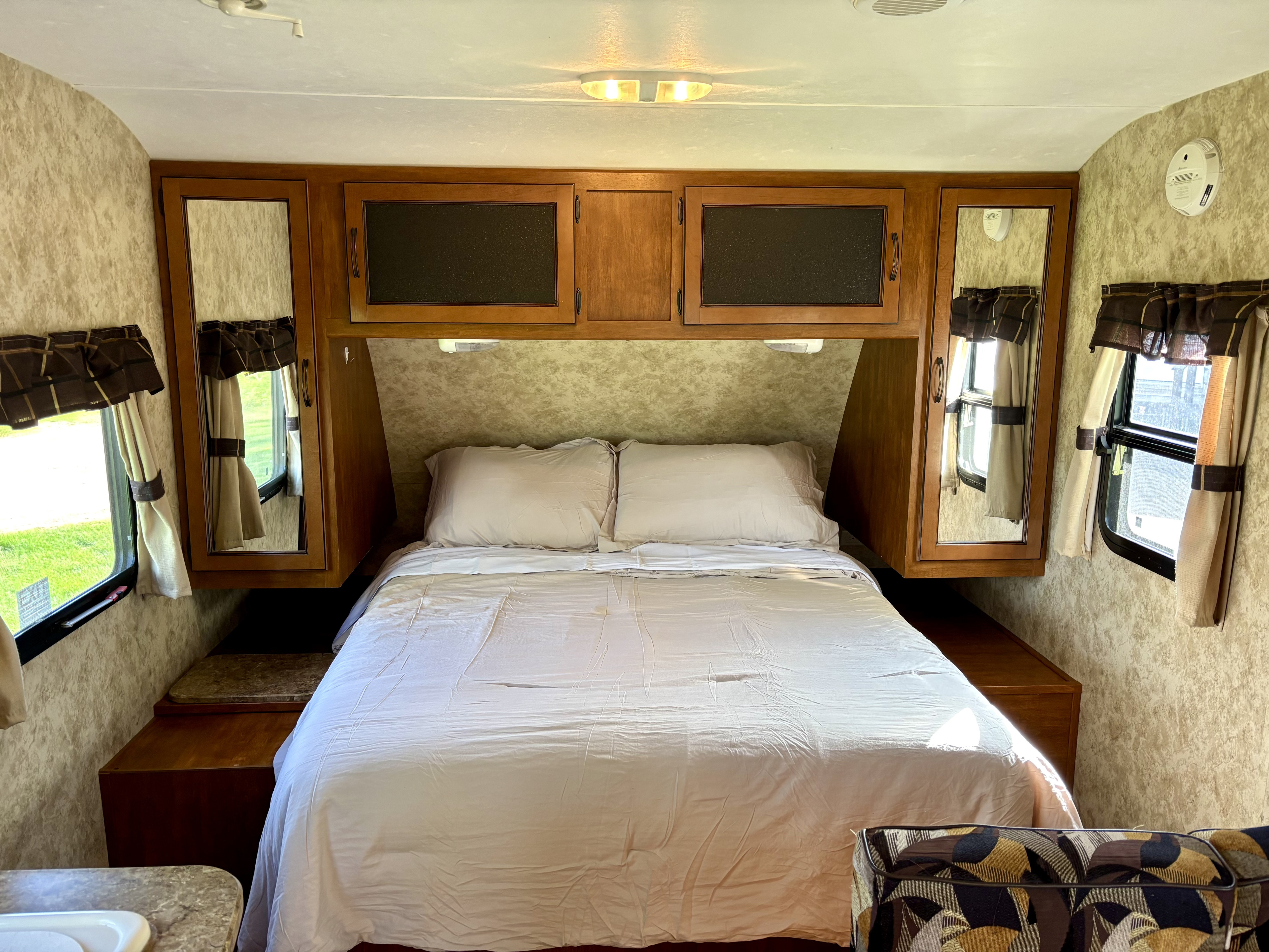 RV rental interior: cozy bedroom with a clean bed, ample overhead cabinets, and windows with natural light.. Keystone RV Bullet Ultra Lite 2012